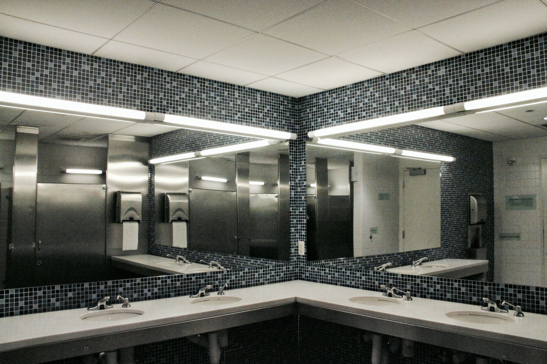 Public restroom with tiled walls, multiple sinks, mirrors, and stainless steel fixtures.