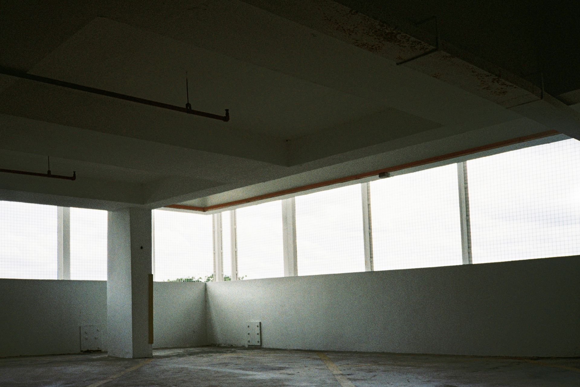 Interior of an empty, white-walled room with large windows along one wall.