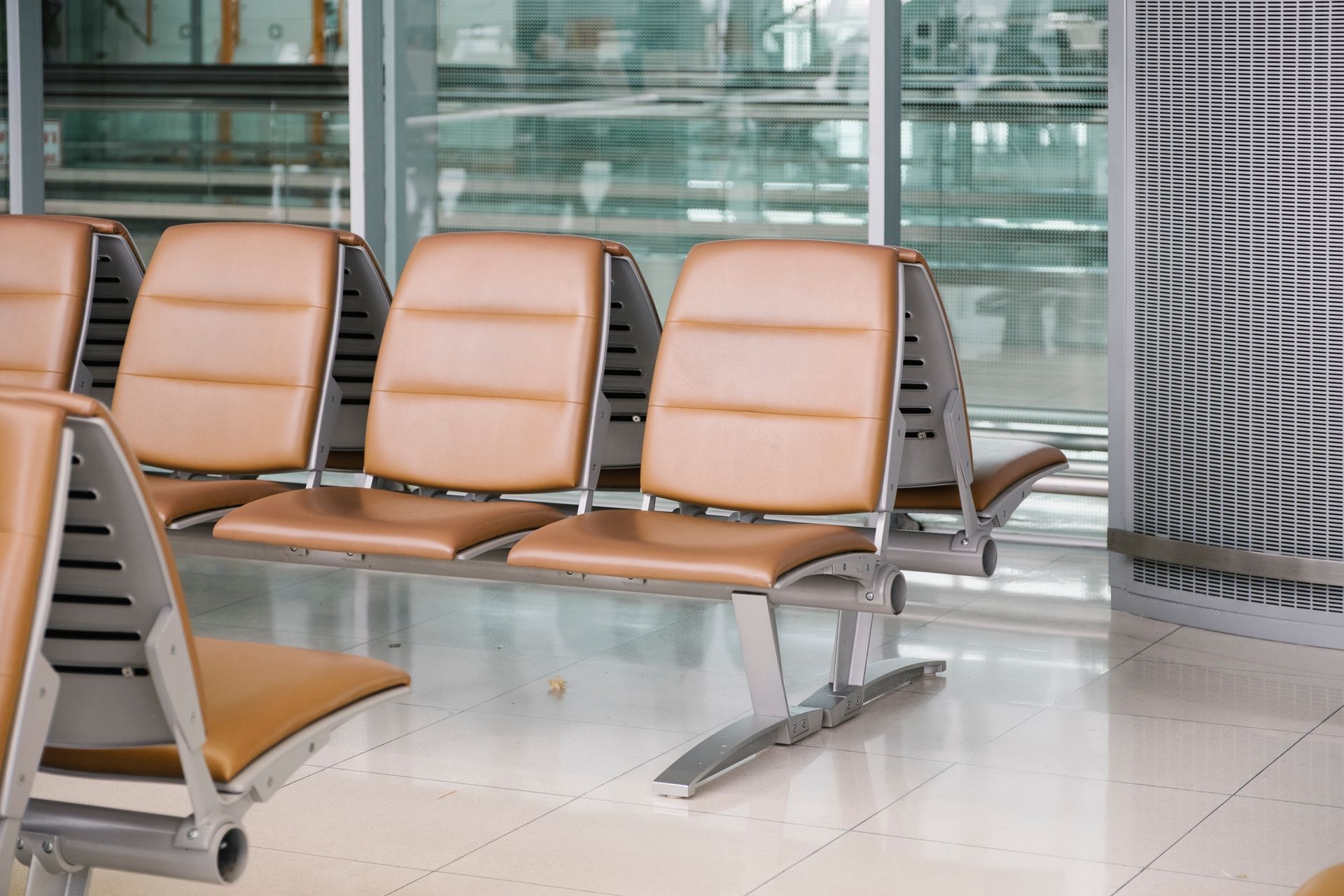 Tan chairs in a waiting area with a reflective, glossy floor and glass windows in background.