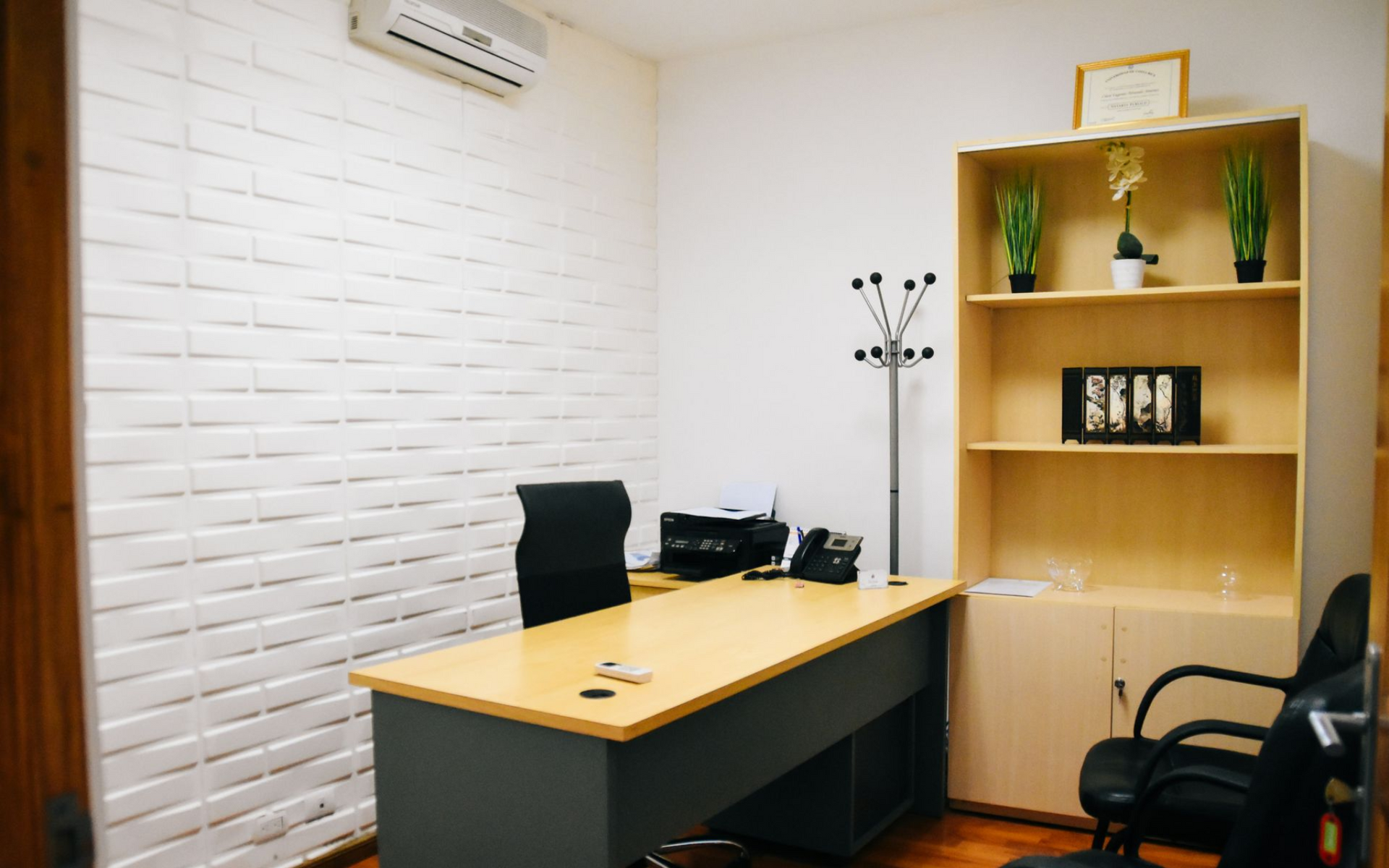 Office interior with desk, shelving unit, and brick wall.
