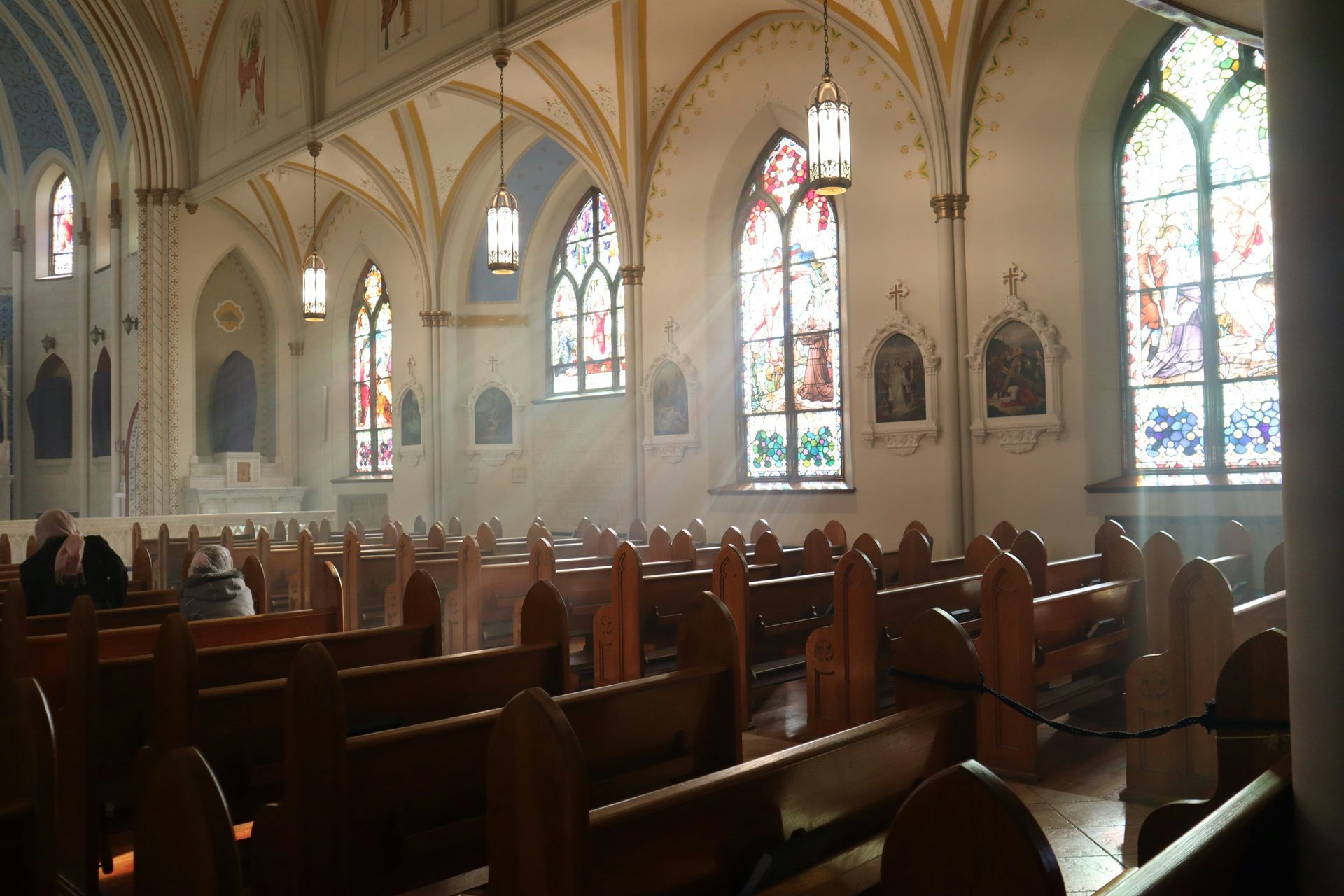 Interior of a church with rows of pews, stained glass windows, and light streaming in.