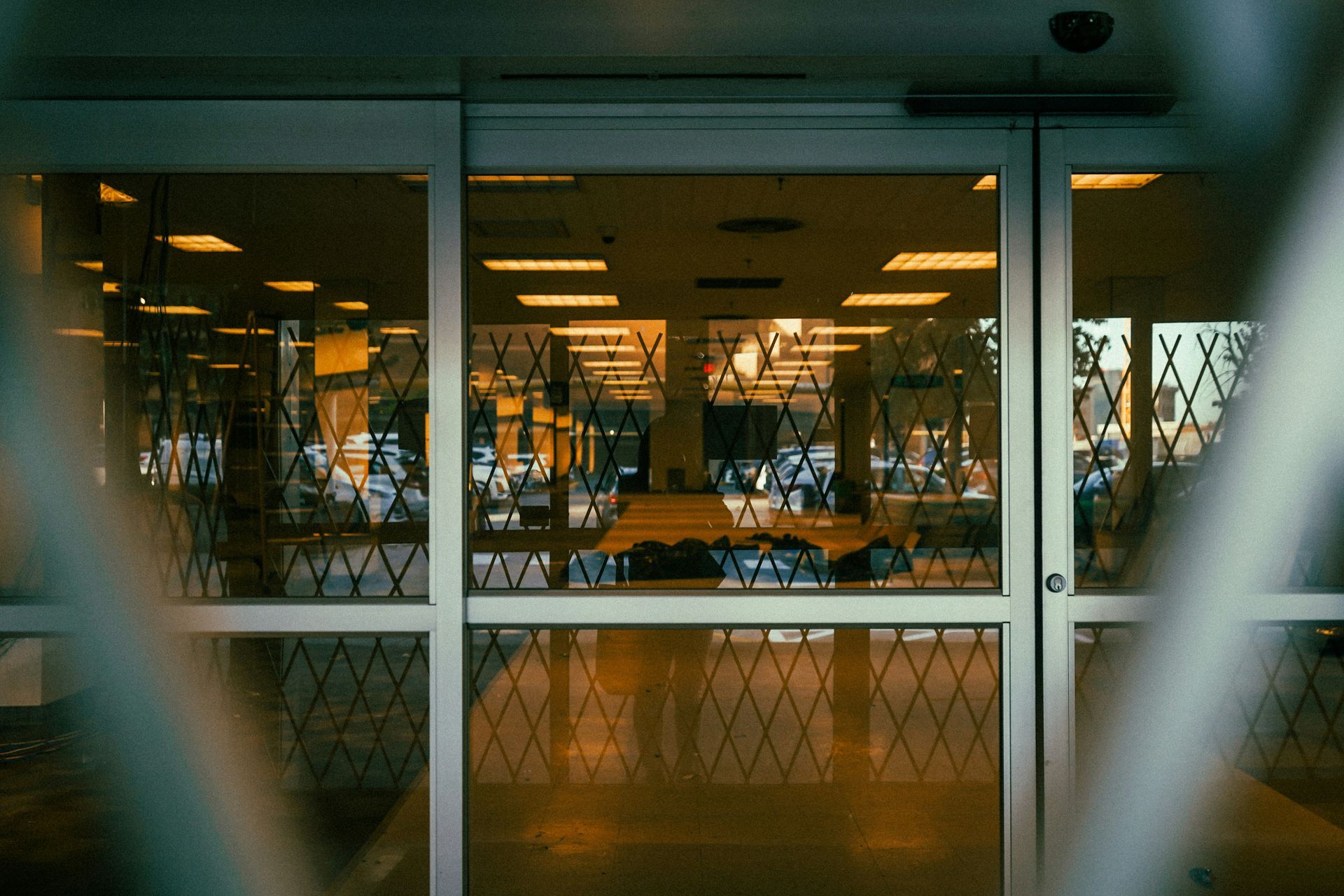 Sliding glass doors with a security gate, reflecting an interior with lights and objects.