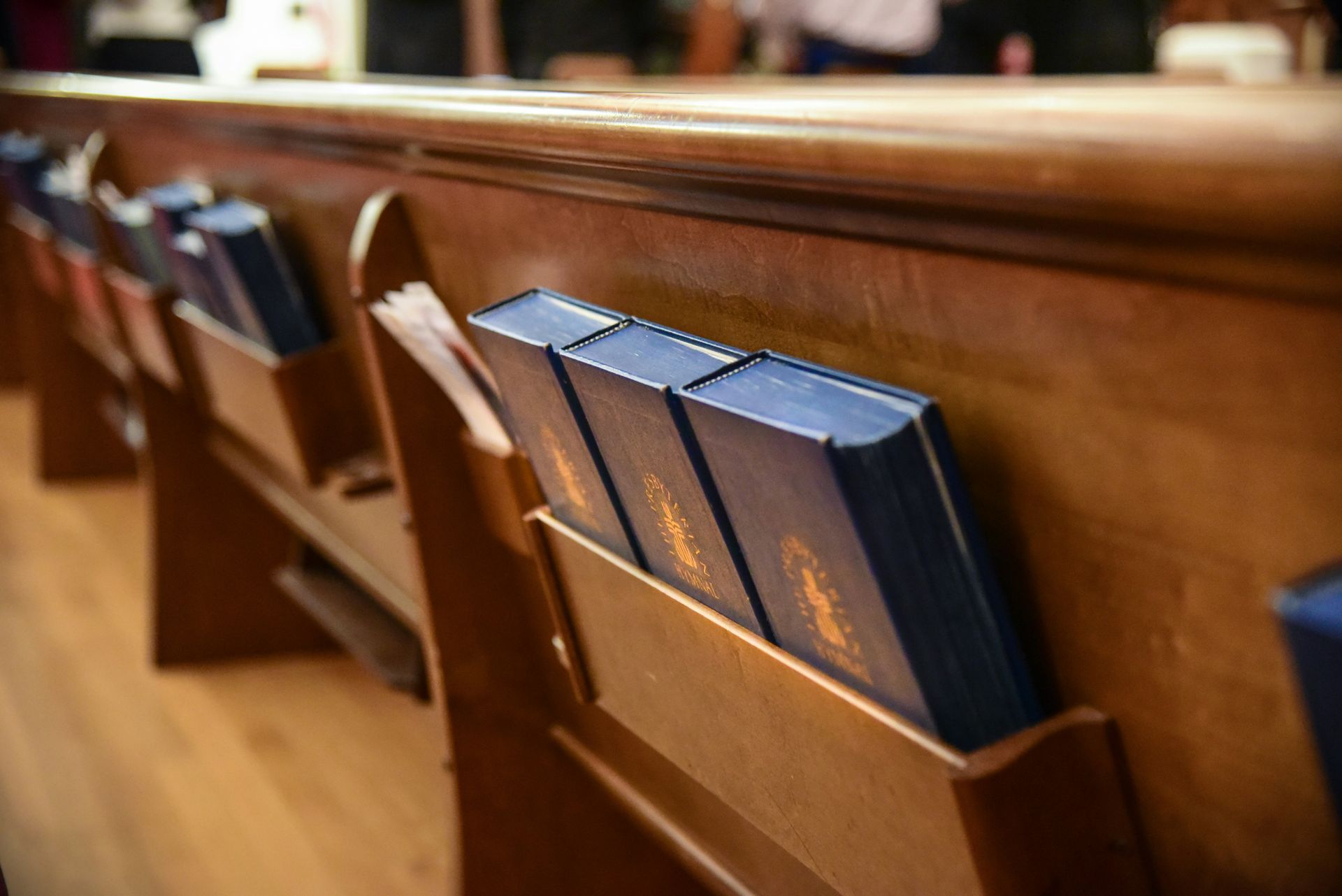 Row of wooden church pews with blue hymnals in the seatbacks.