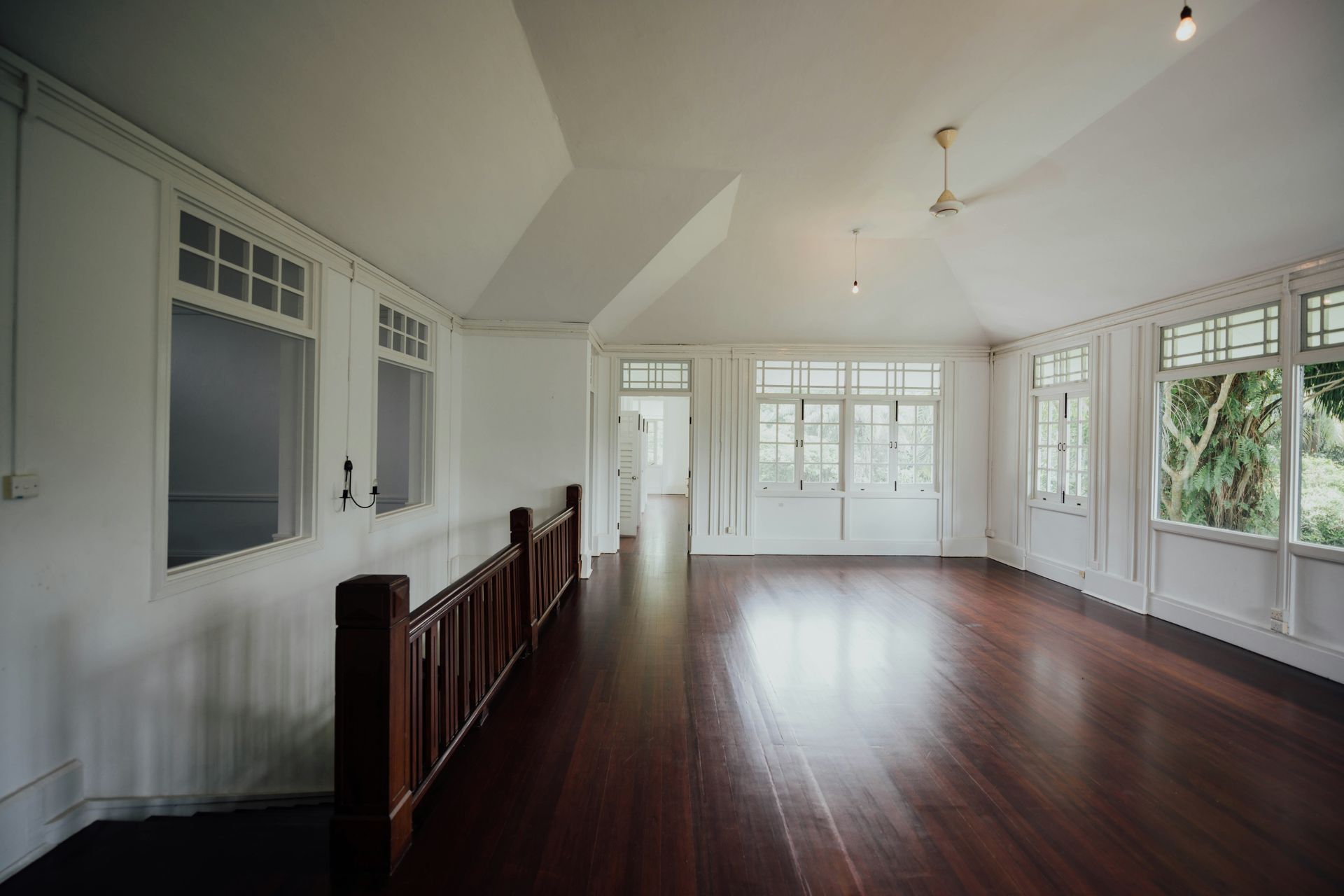 Interior of a bright, empty room with dark wood floors, white walls, and large windows.