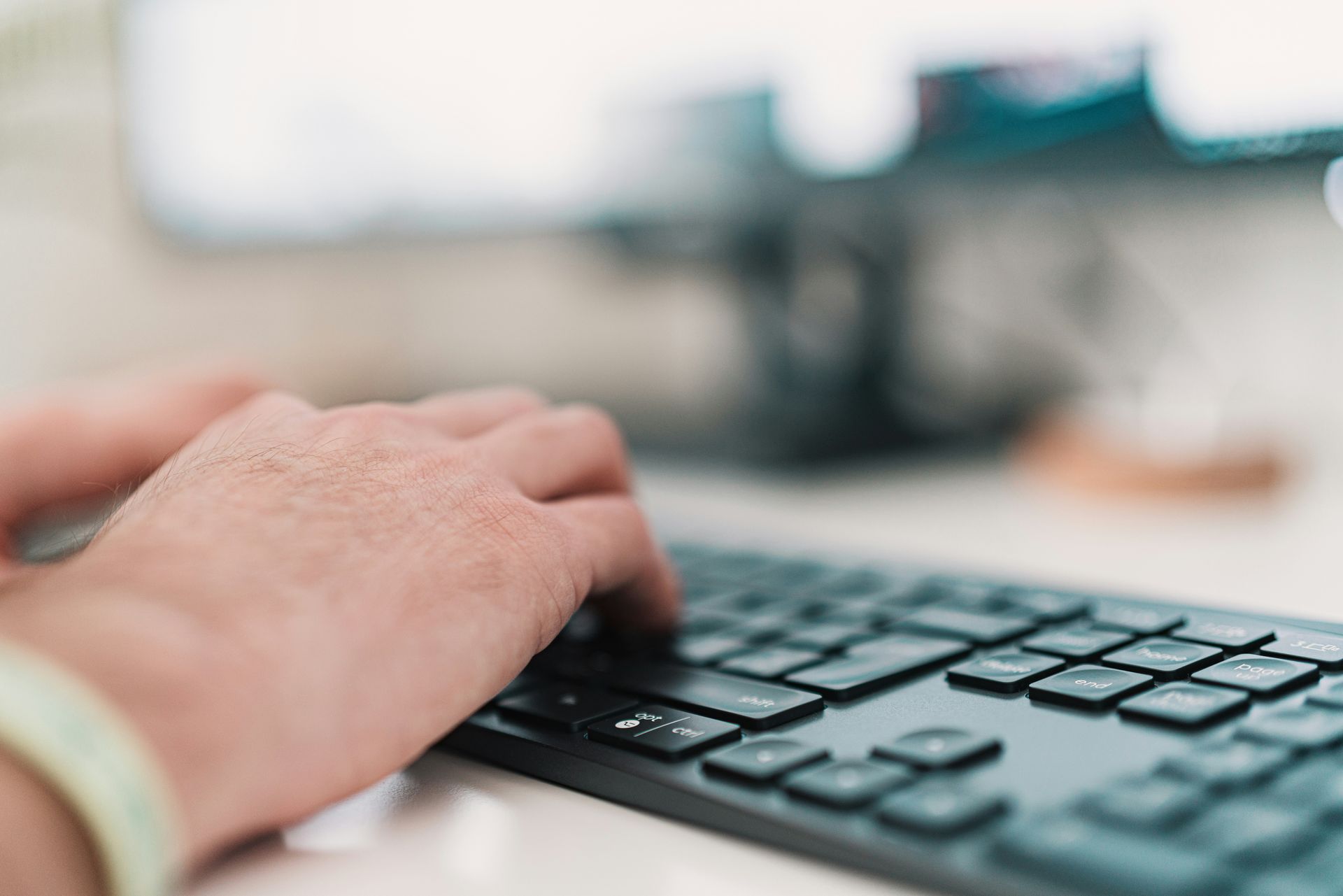 Hands typing on a black keyboard, in front of a computer monitor.