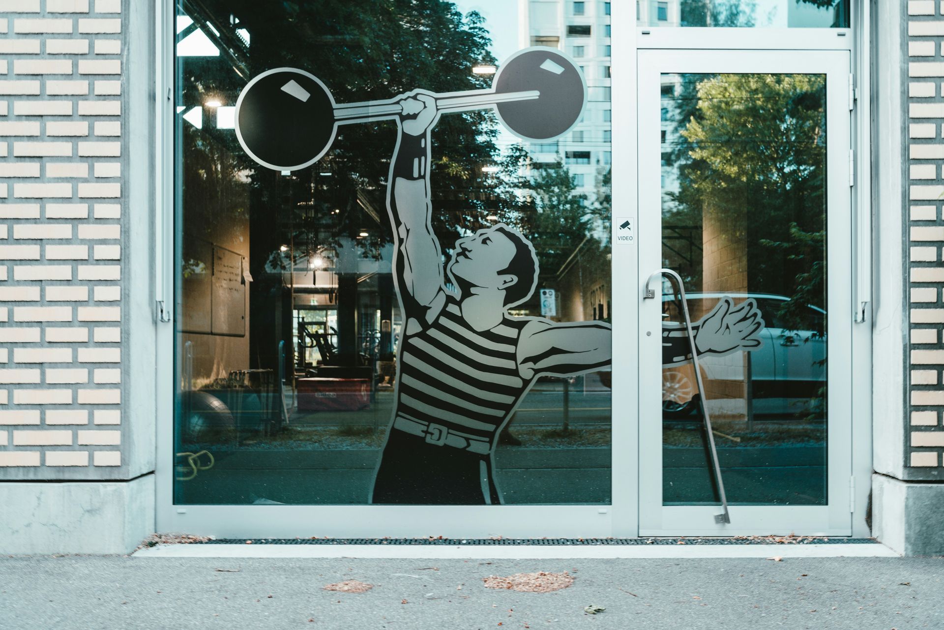 Gym door with a lifter silhouette, holding a barbell overhead. Reflective glass.