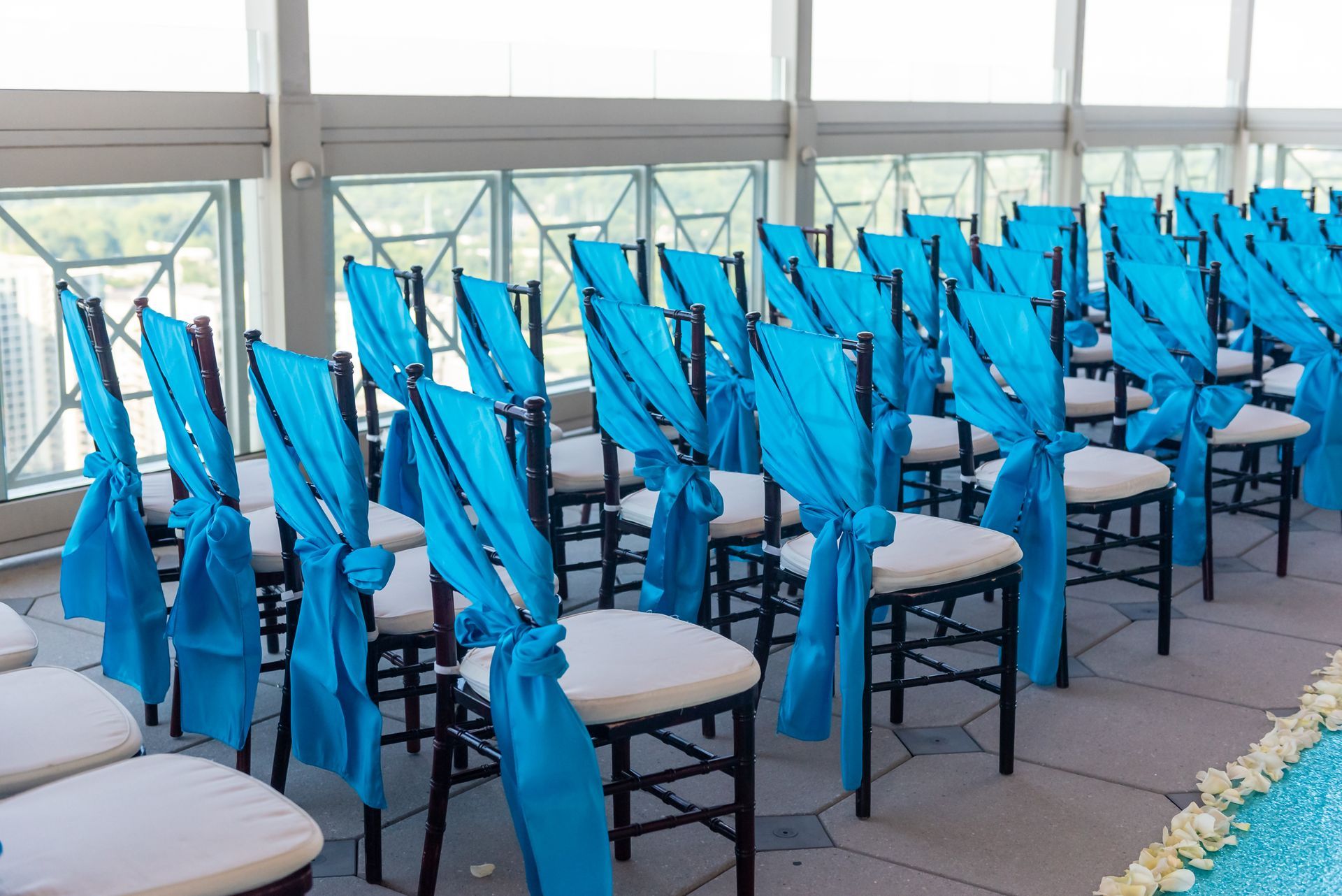 Rows of black chairs with white seats and turquoise fabric tied on the backs, set up for an outdoor event.