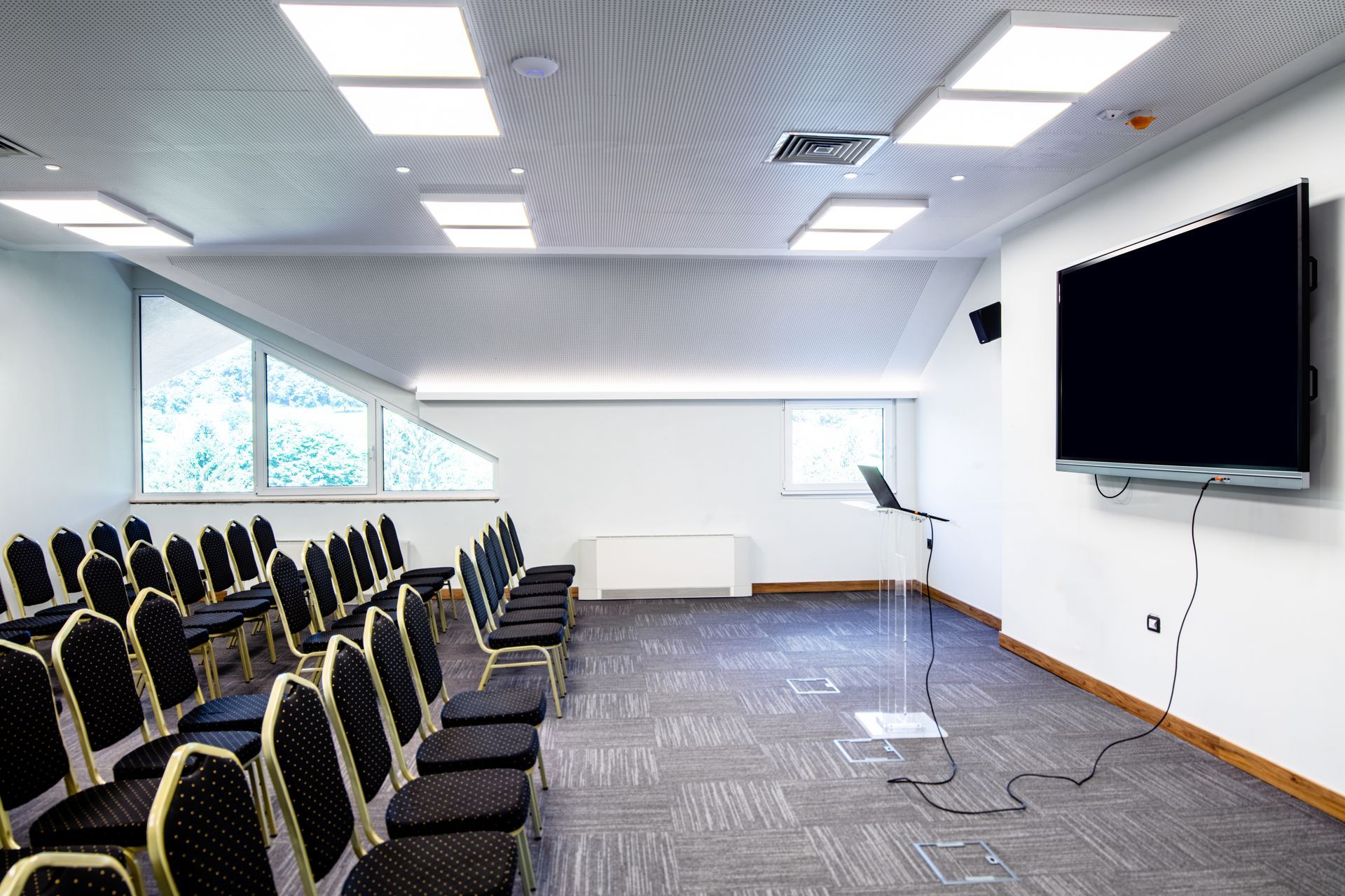 Empty conference room with rows of chairs, large screen, and podium.