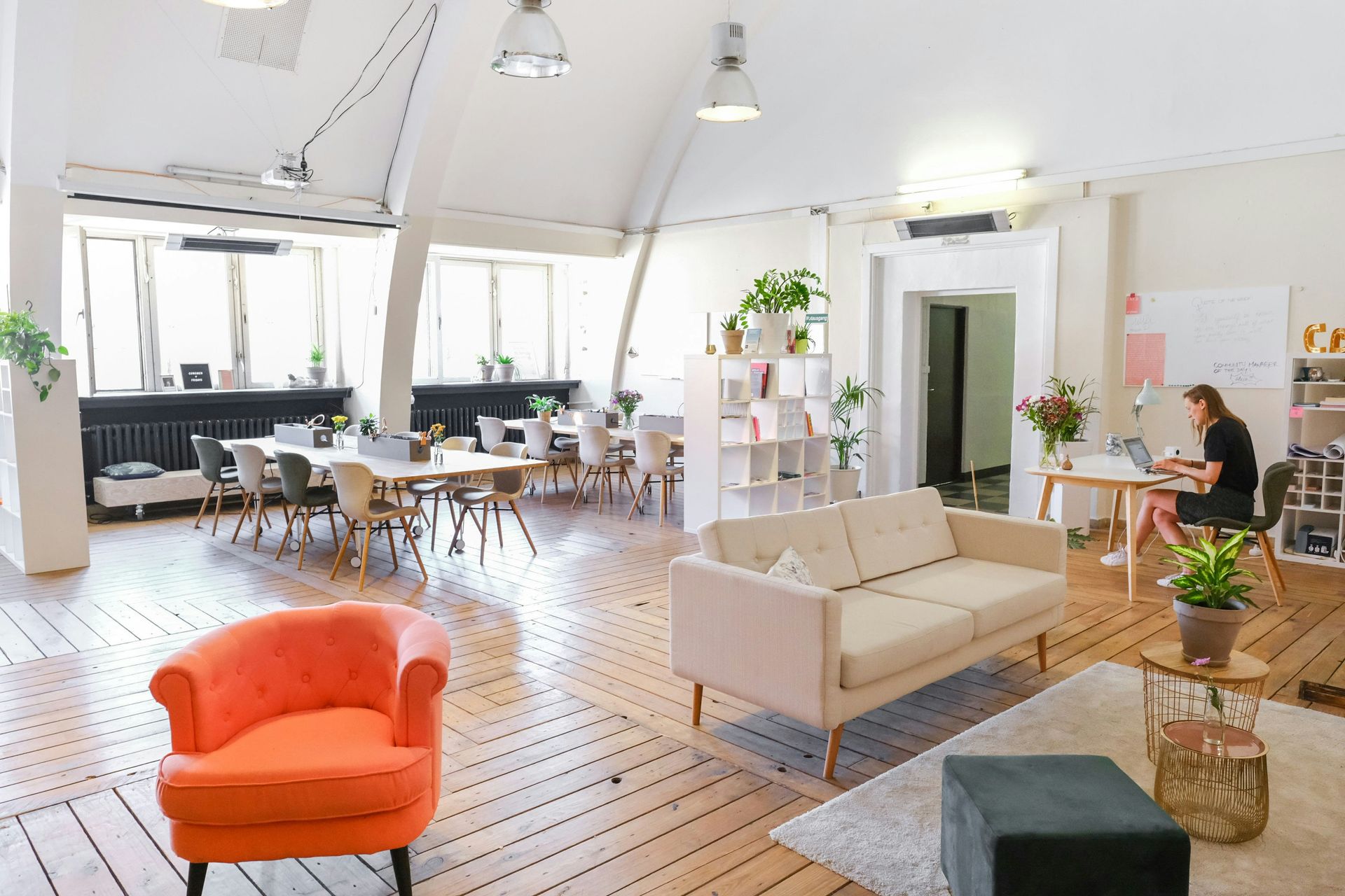 Bright co-working space with seating areas, long table, and person working at a desk.