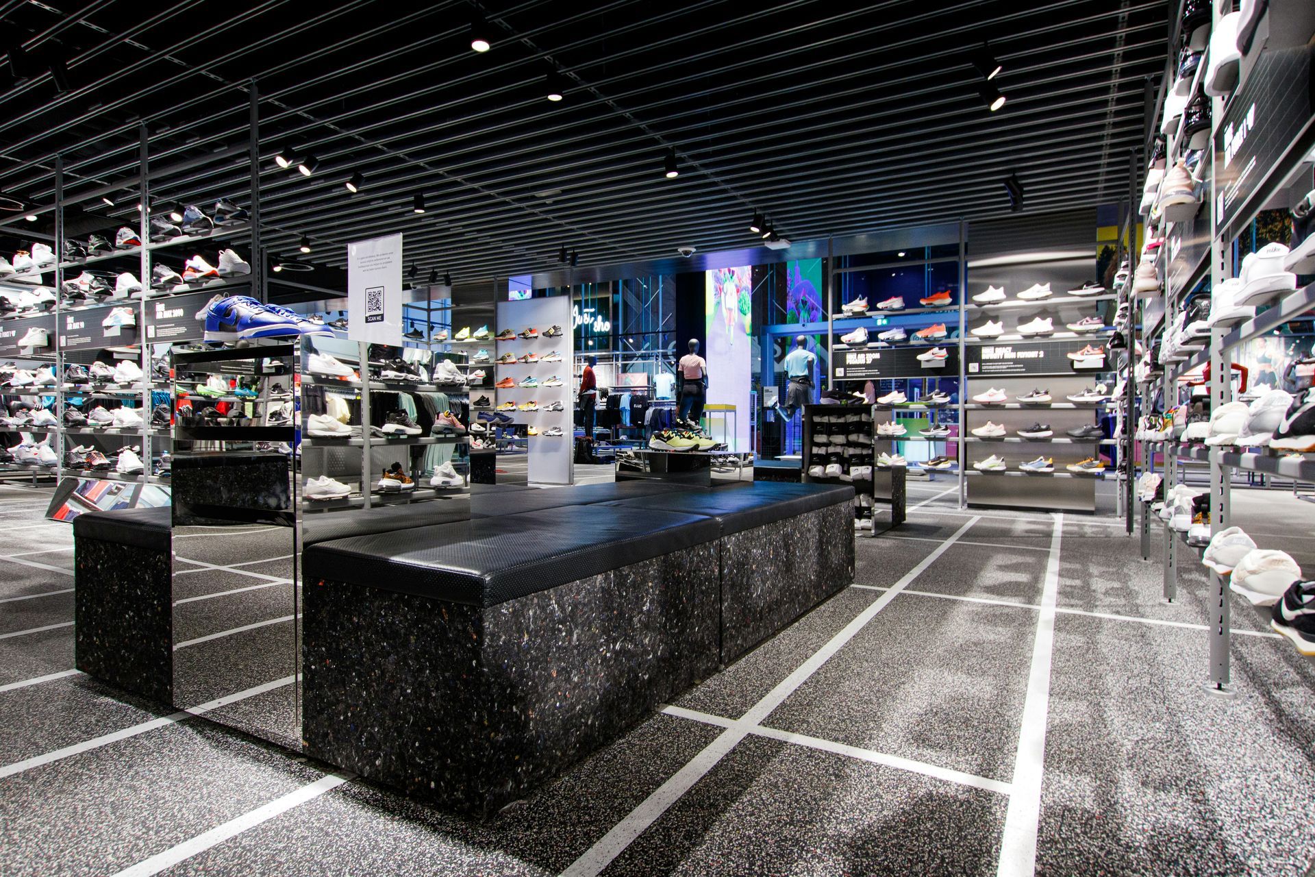 Shoe store interior with displays of sneakers on walls and a central display island, grey and black color scheme.