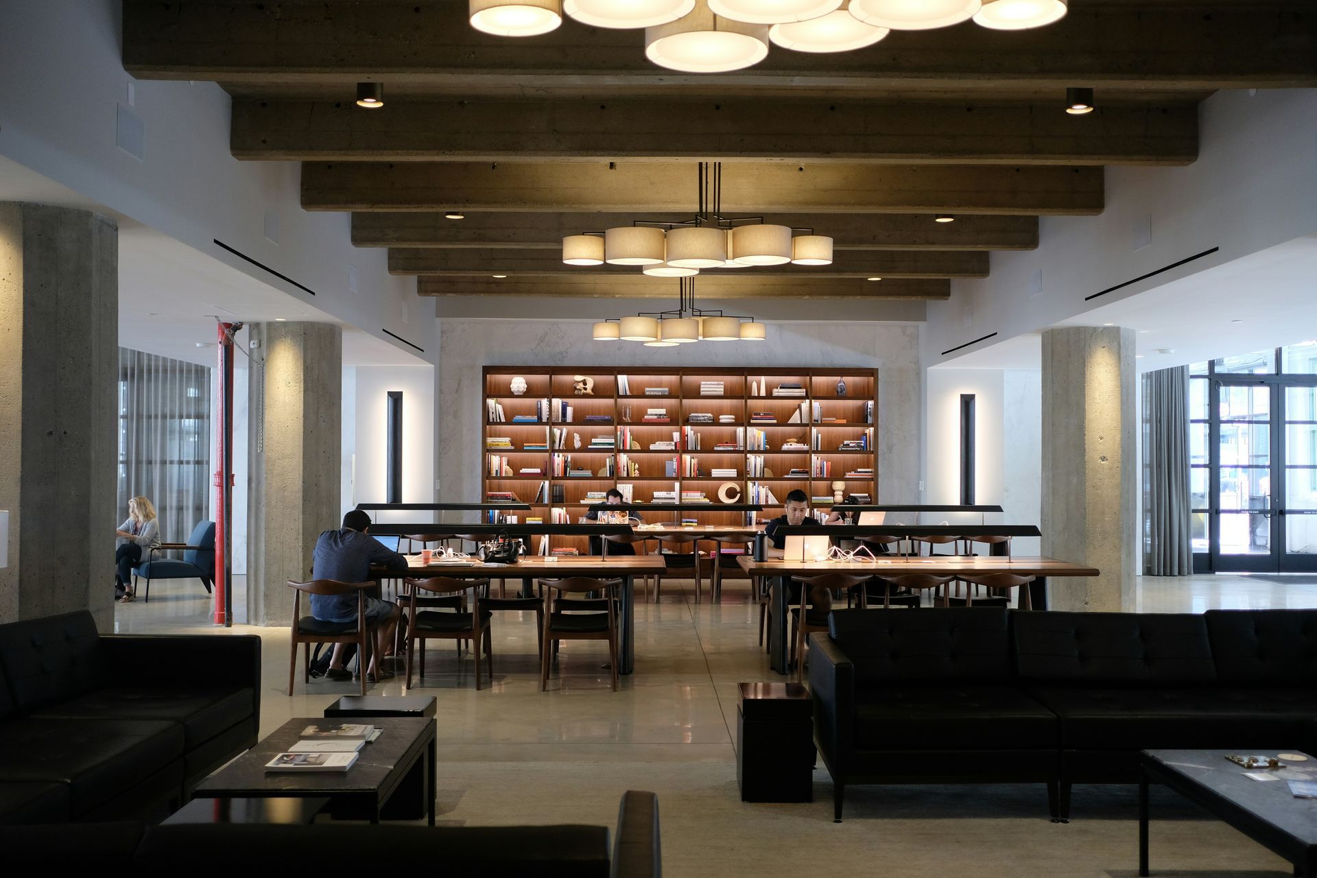 Spacious library interior with reading tables, bookshelves, and couches. People working and relaxing.