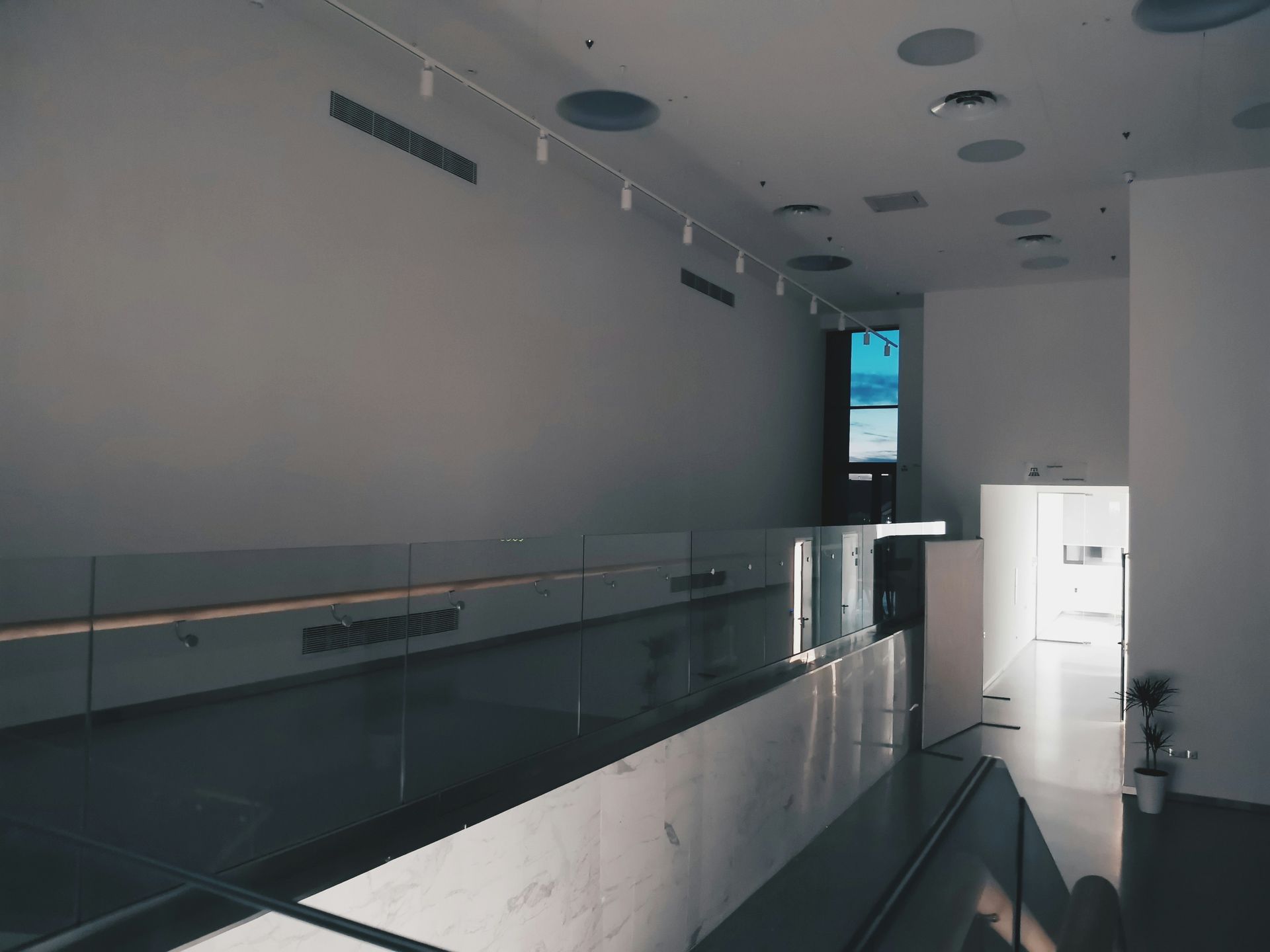Modern, bright interior with long, marble counter and glass railing. Tall wall with blue light.