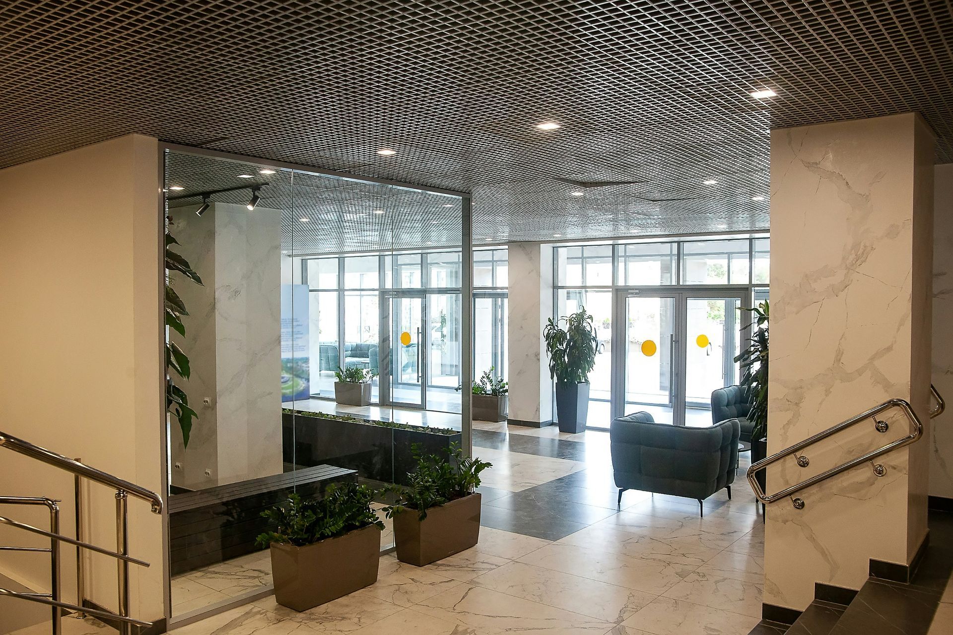 Modern lobby with marble floors and columns, plants, glass doors, and mirrored wall.