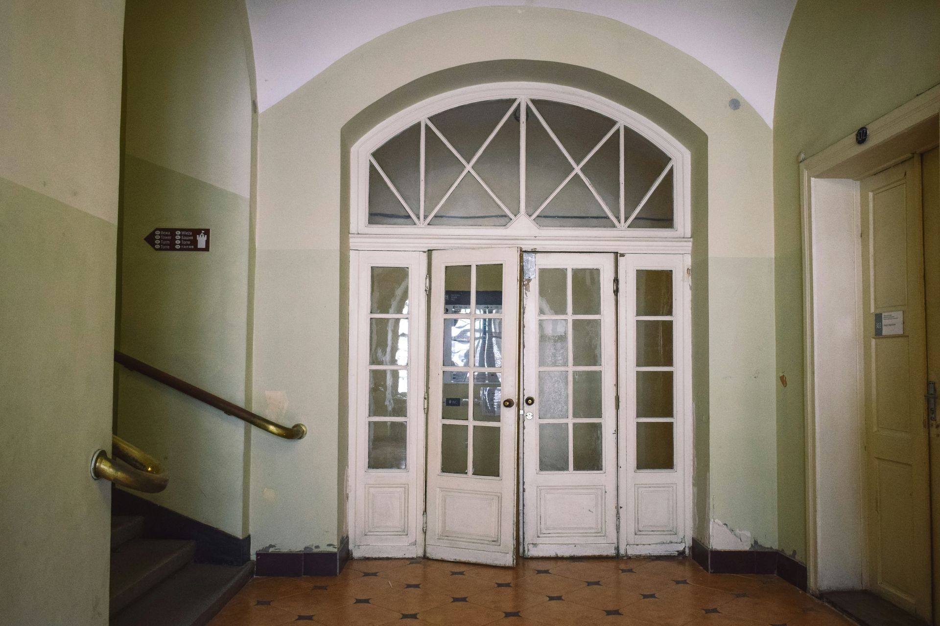 Interior hallway with arched doorway and glass doors. Pale green walls, tile floor, stairs, and elevator.