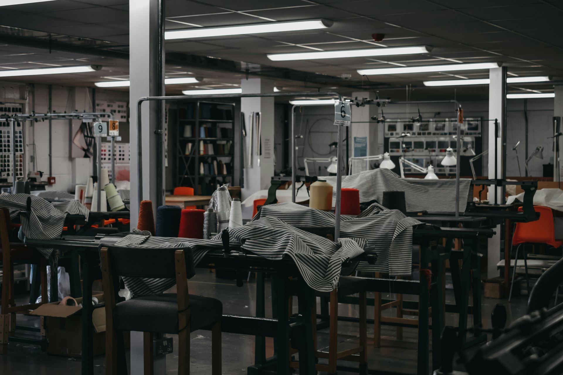 Interior view of a sewing workshop with tables, spools of thread, and overhead lighting.