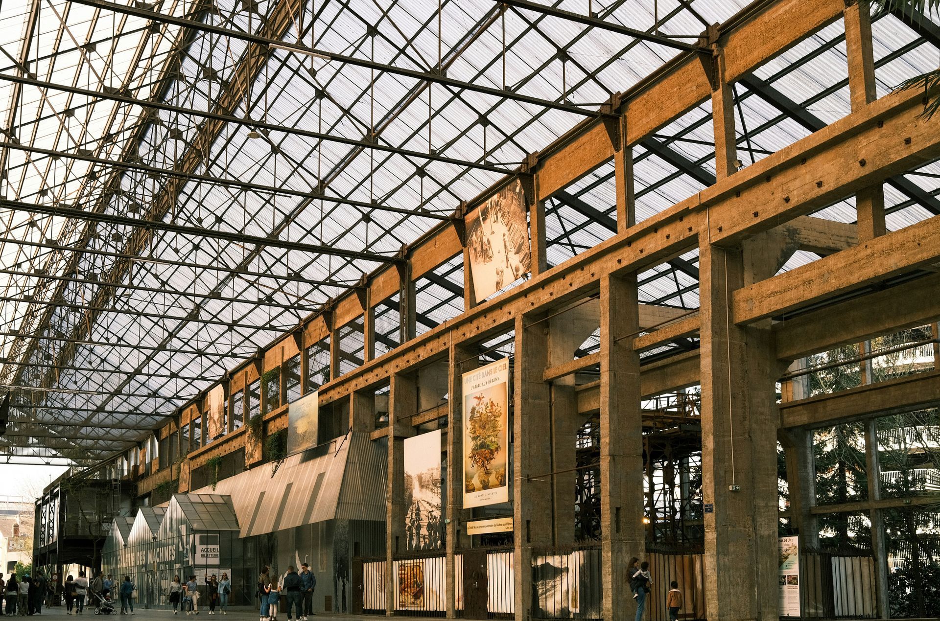 Large hall with wood beams, glass roof, and paintings on the walls; people are visible inside.