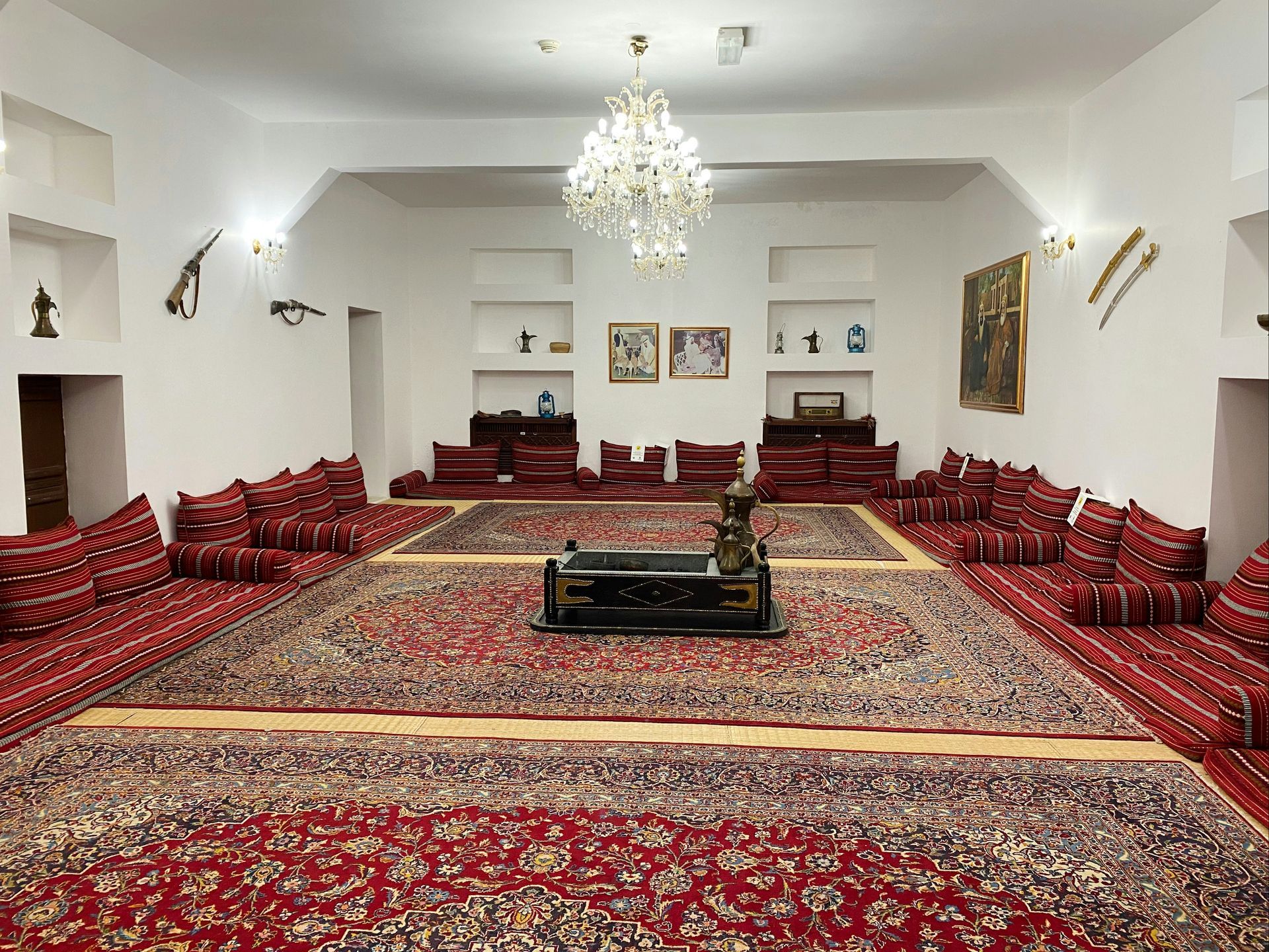 A room with red rugs and cushions, traditional decor, a chandelier, and wall art.