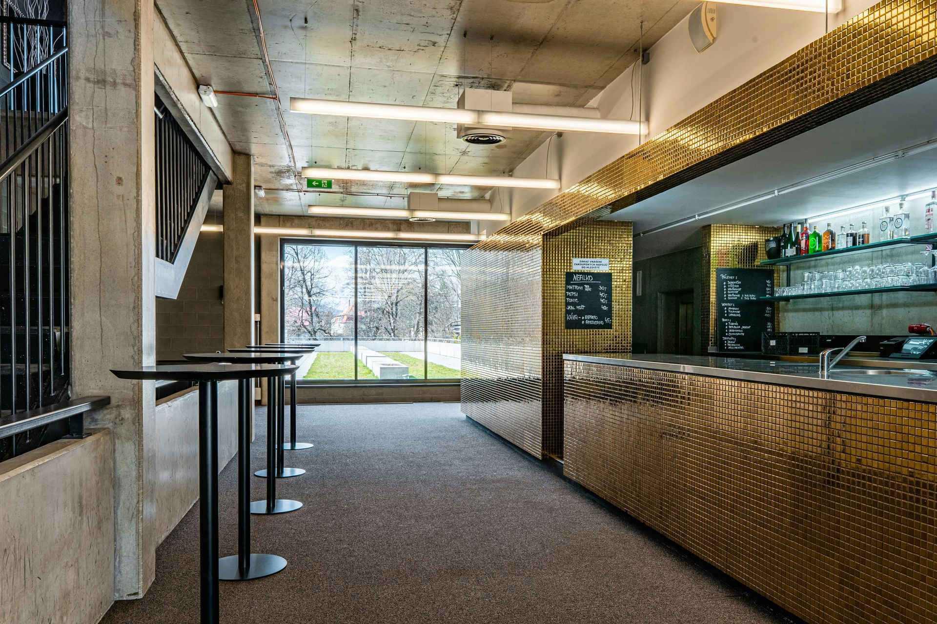 Bar area with gold facade, tall tables, and window overlooking a green area.