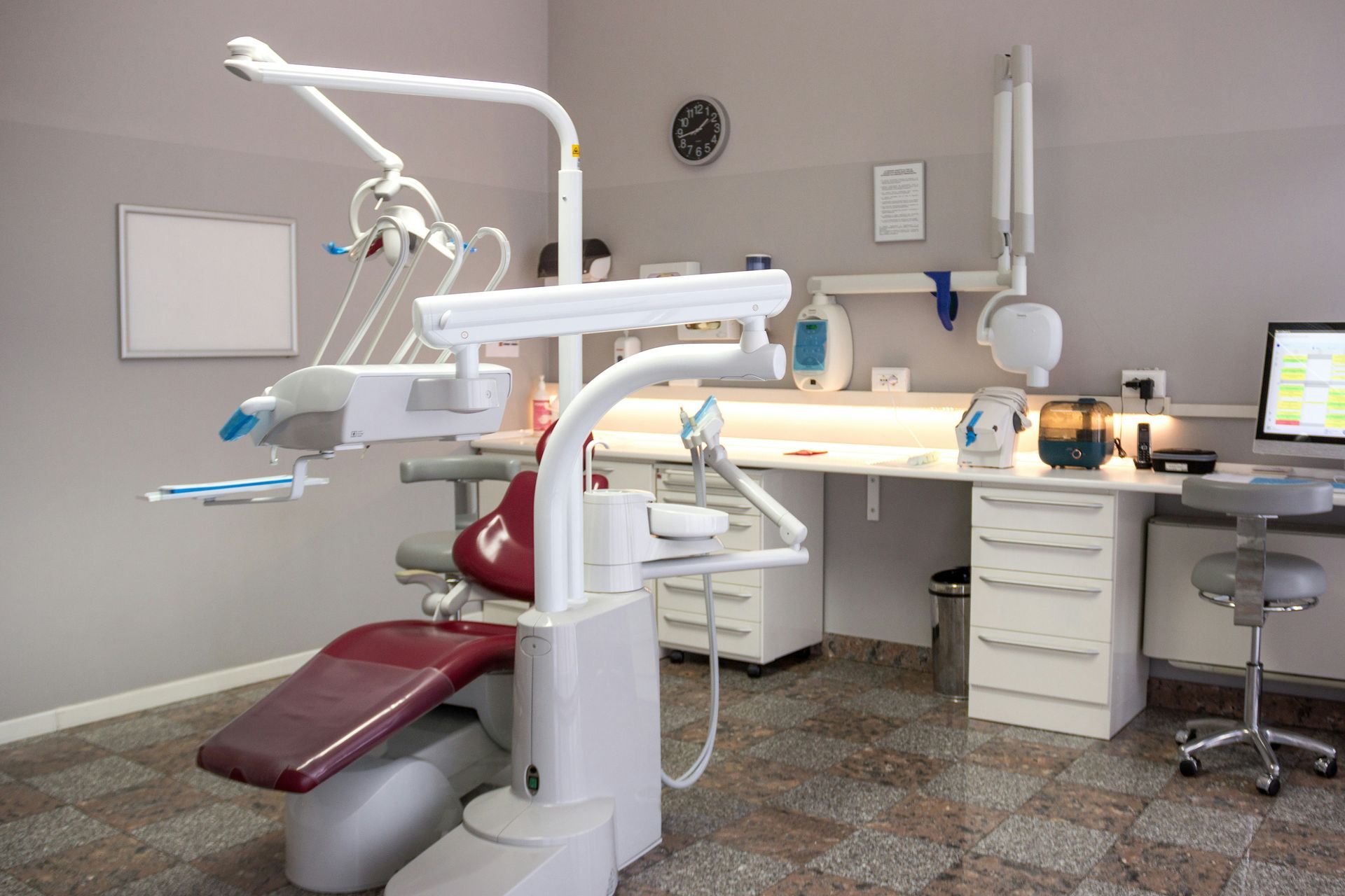Dental office interior with burgundy chair, equipment, and desk.
