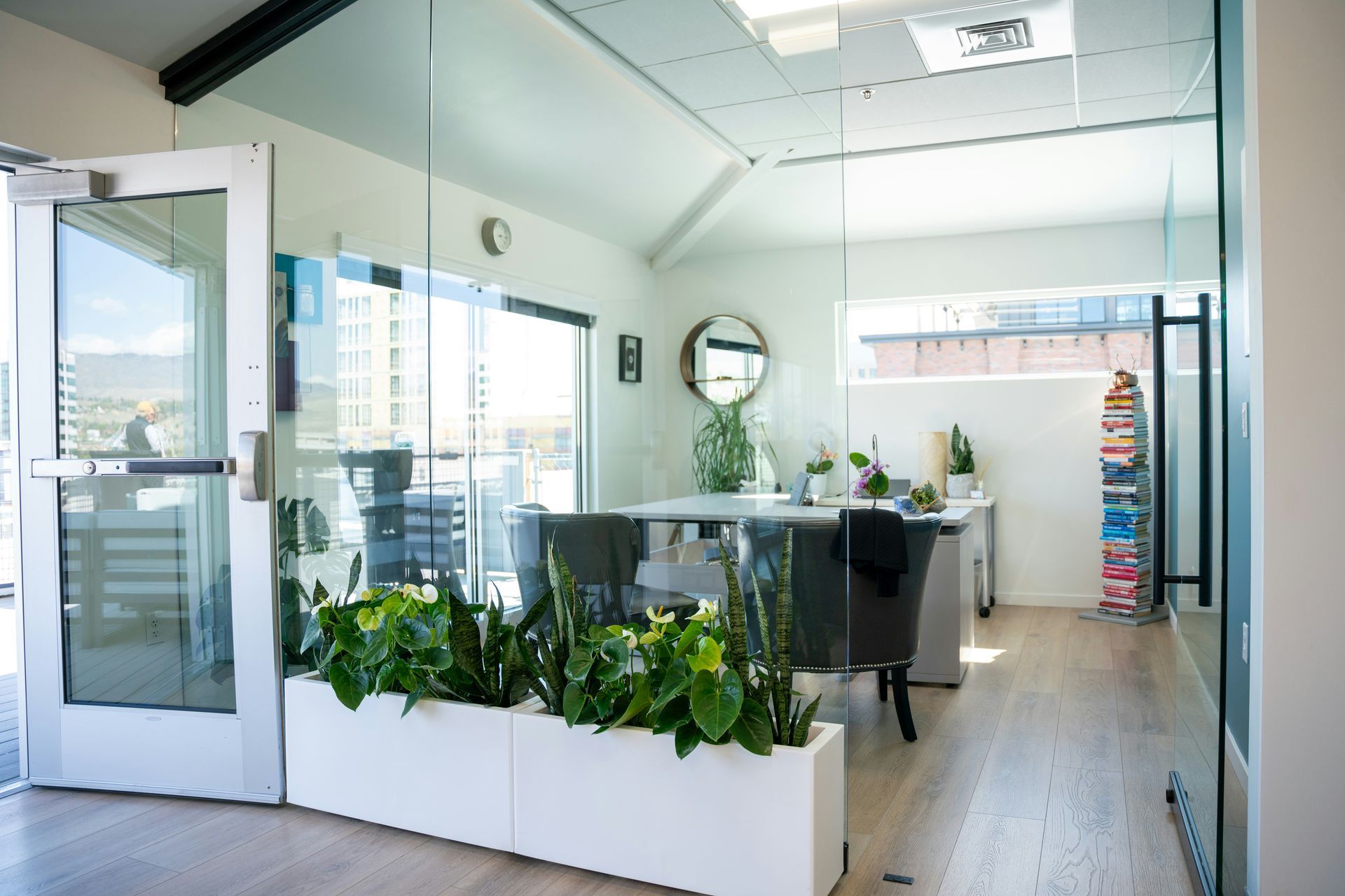 Office interior with glass walls, plants, desk, chairs, and door.
