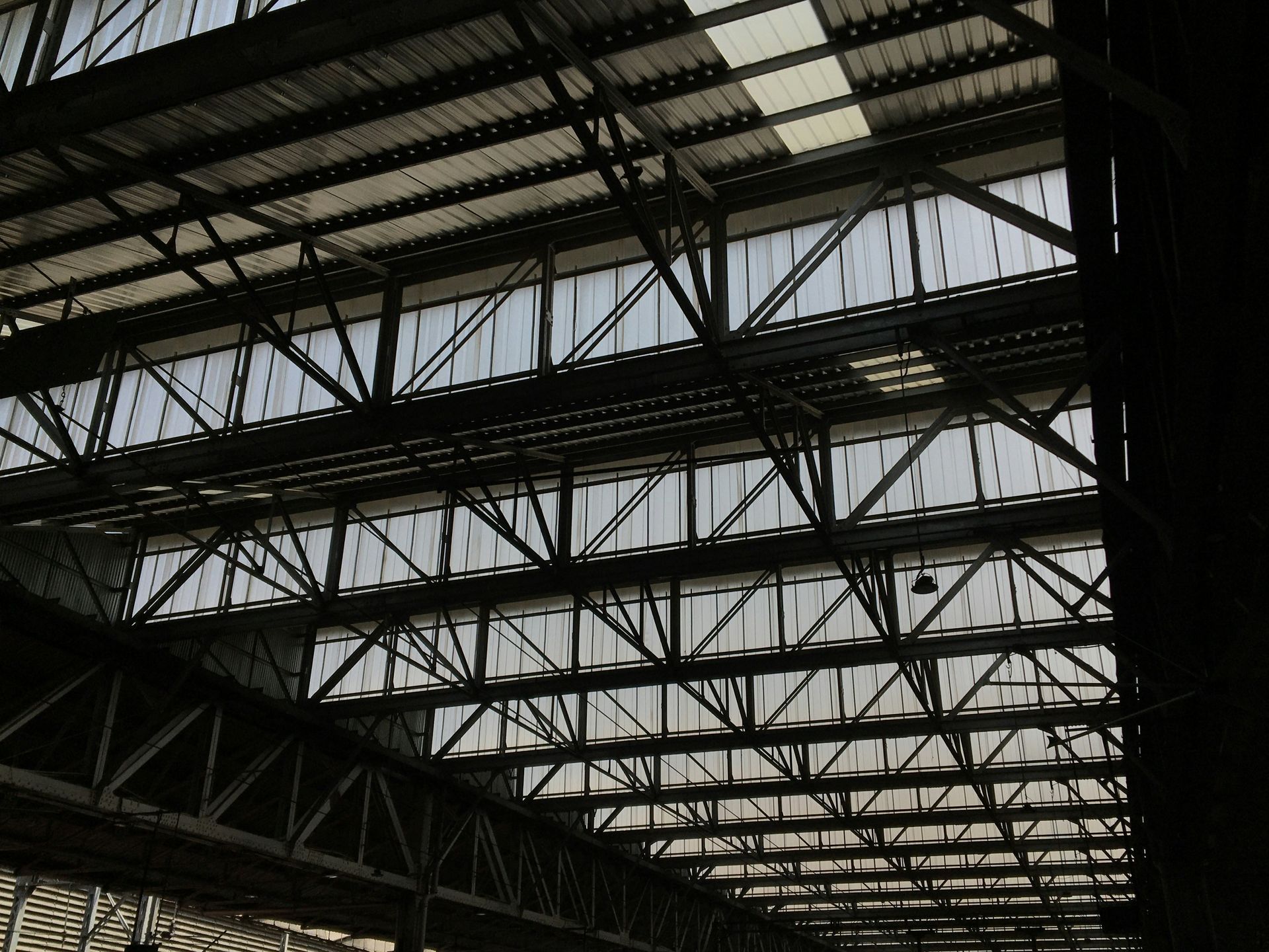 Metal beams and panels form a ceiling in a factory or warehouse; natural light shines through the translucent panels.
