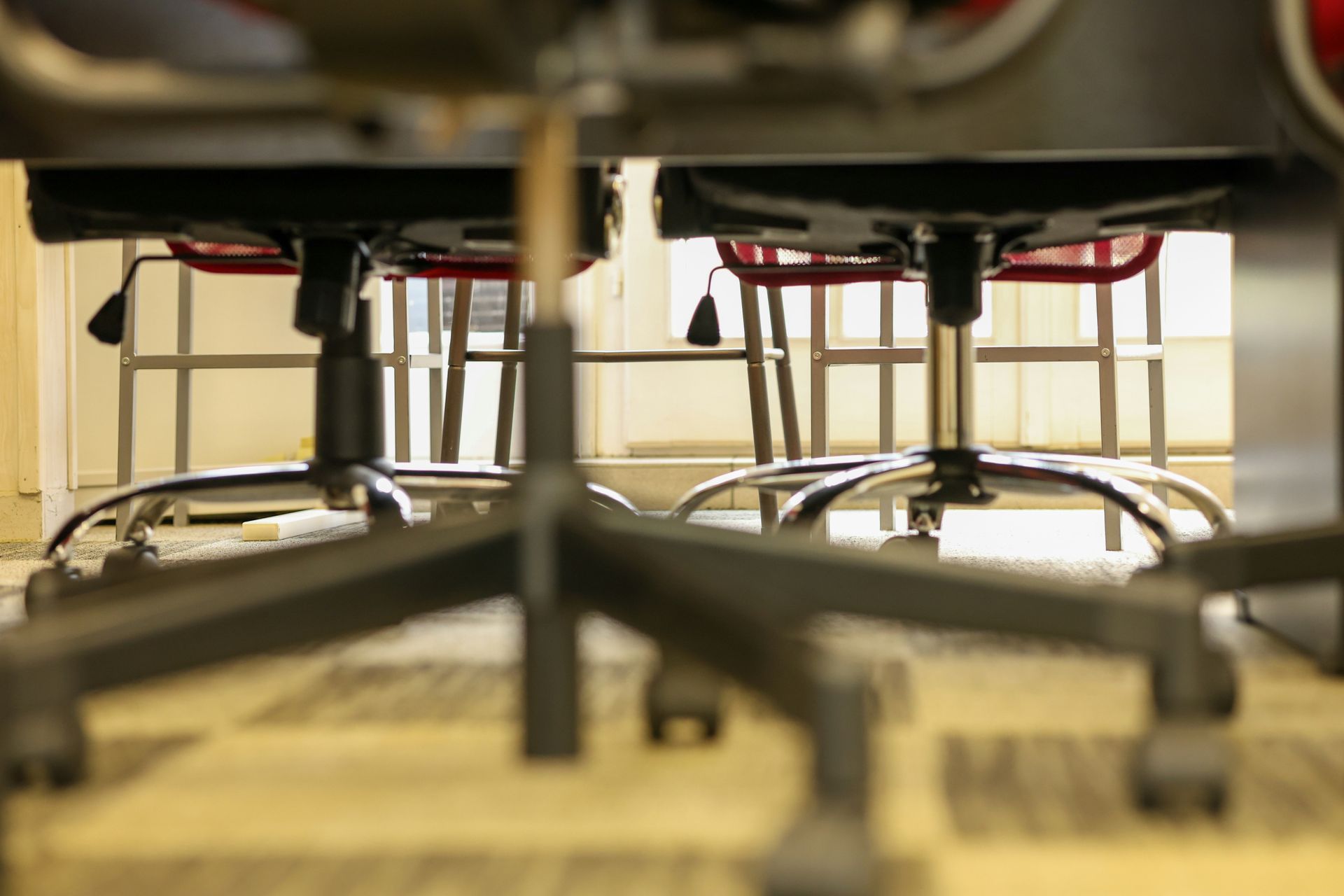 Two office chairs with red backs and black bases, viewed from below.