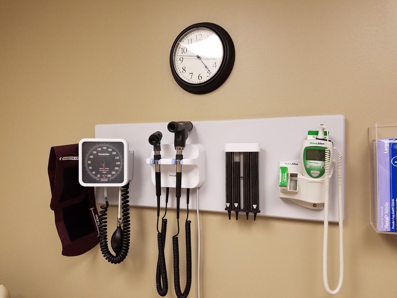Medical exam tools mounted on wall, including blood pressure gauge, otoscope, and thermometer.