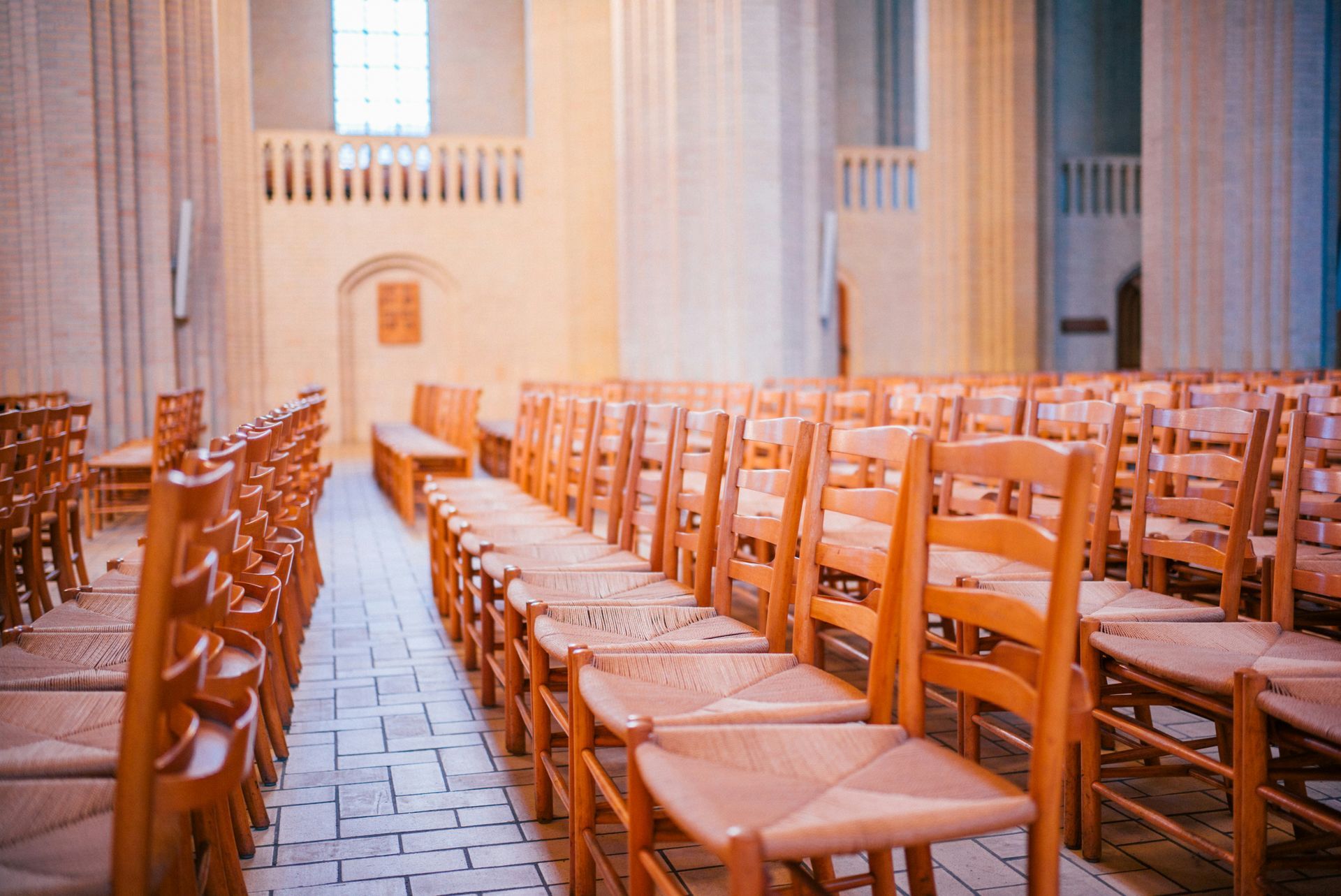 Rows of empty wooden chairs in a light-filled church interior.