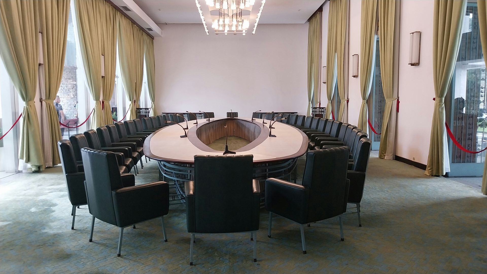 Round conference table with black chairs, in a bright room with light green curtains.