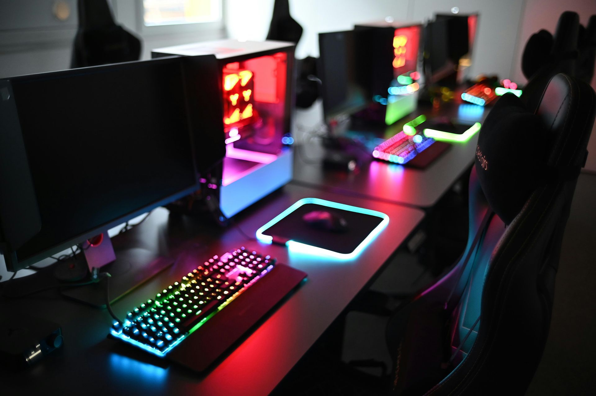 Gaming computers with colorful keyboards and lighting in a dimly lit room.