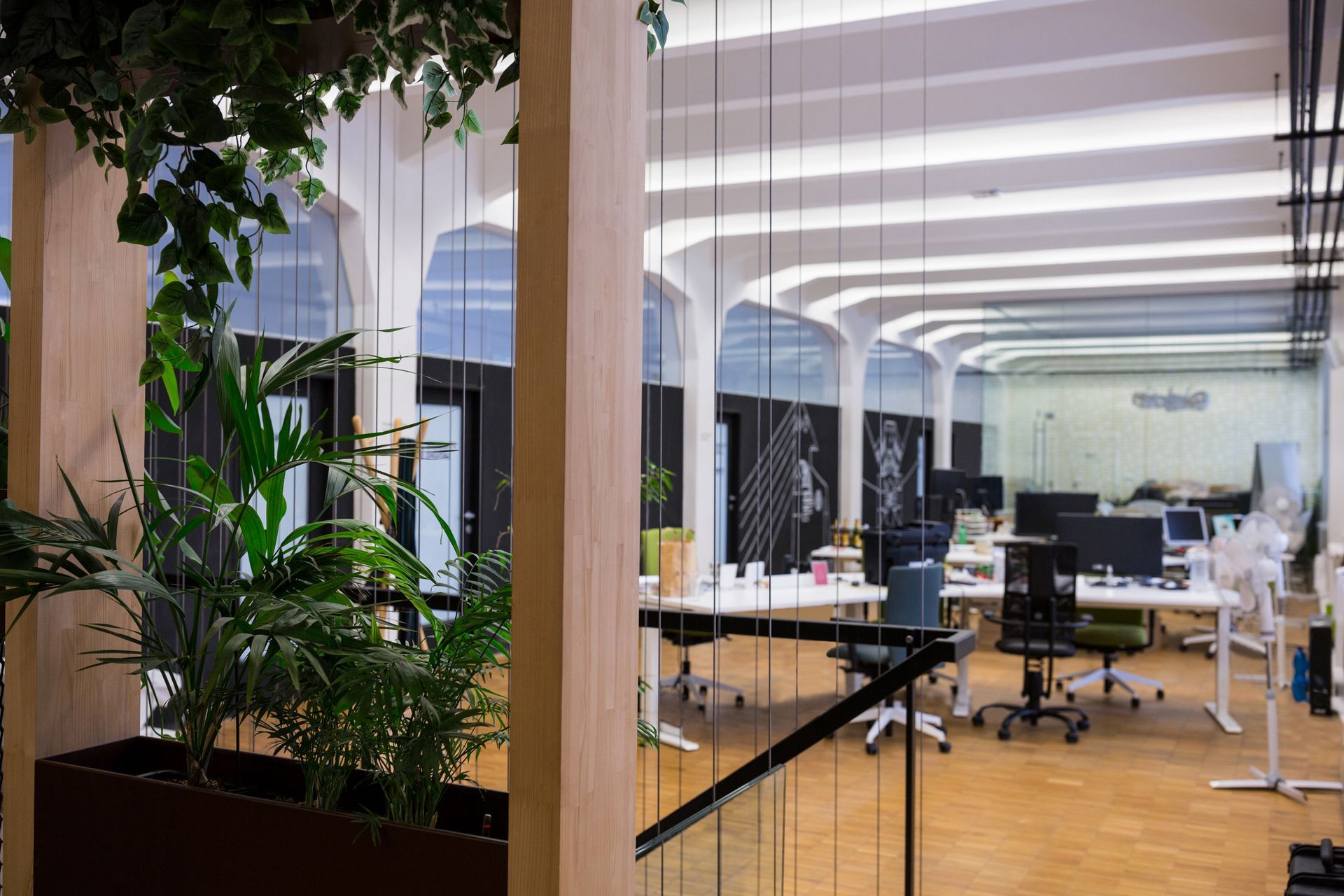 Office interior with plants, workstations, arched windows, and wood pillars.
