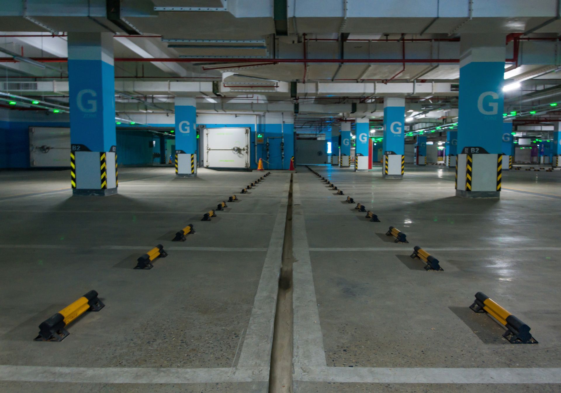 Empty blue and gray parking garage with marked spaces, pillars, and overhead lights.