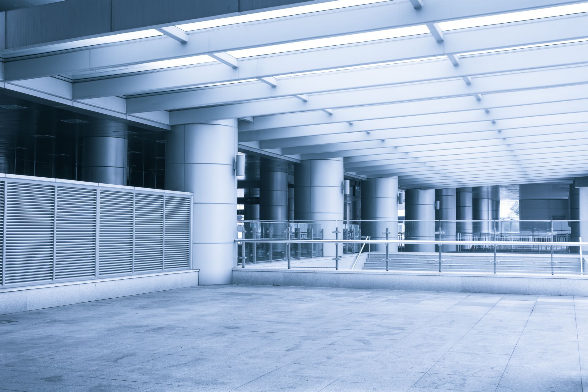 Blue-toned view of an empty modern interior with pillars, a patterned wall, and a long, open hallway.