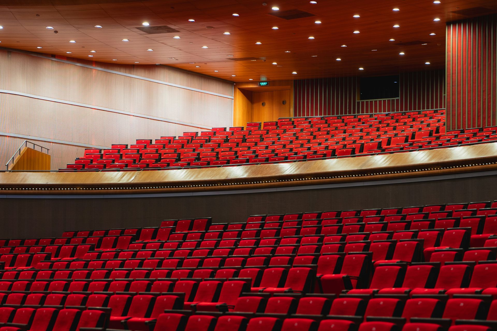 Rows of empty red seats in a theater auditorium, with wood paneling and lighting.