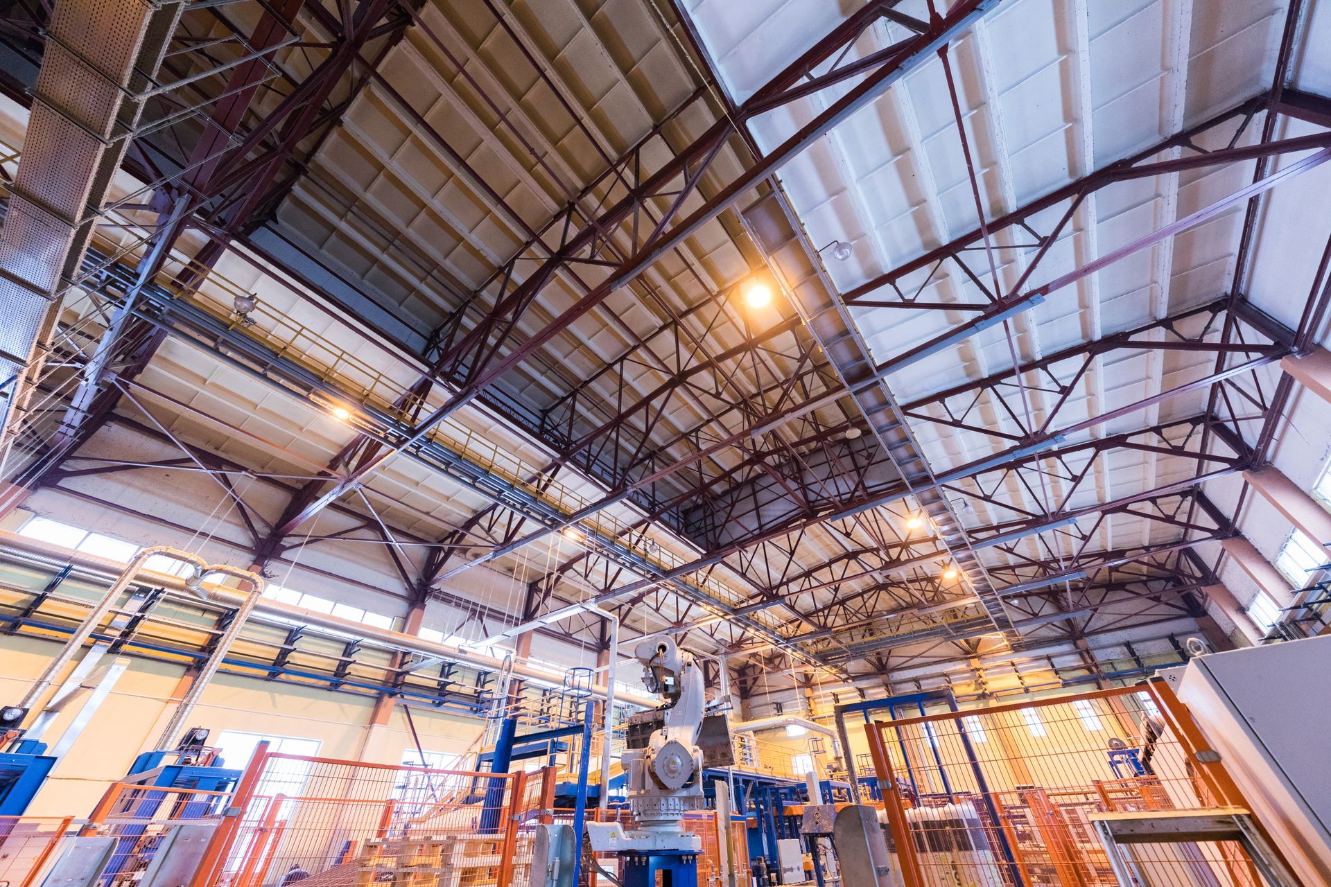 Factory interior with exposed steel beams supporting a high ceiling. Equipment and pipes are visible below.