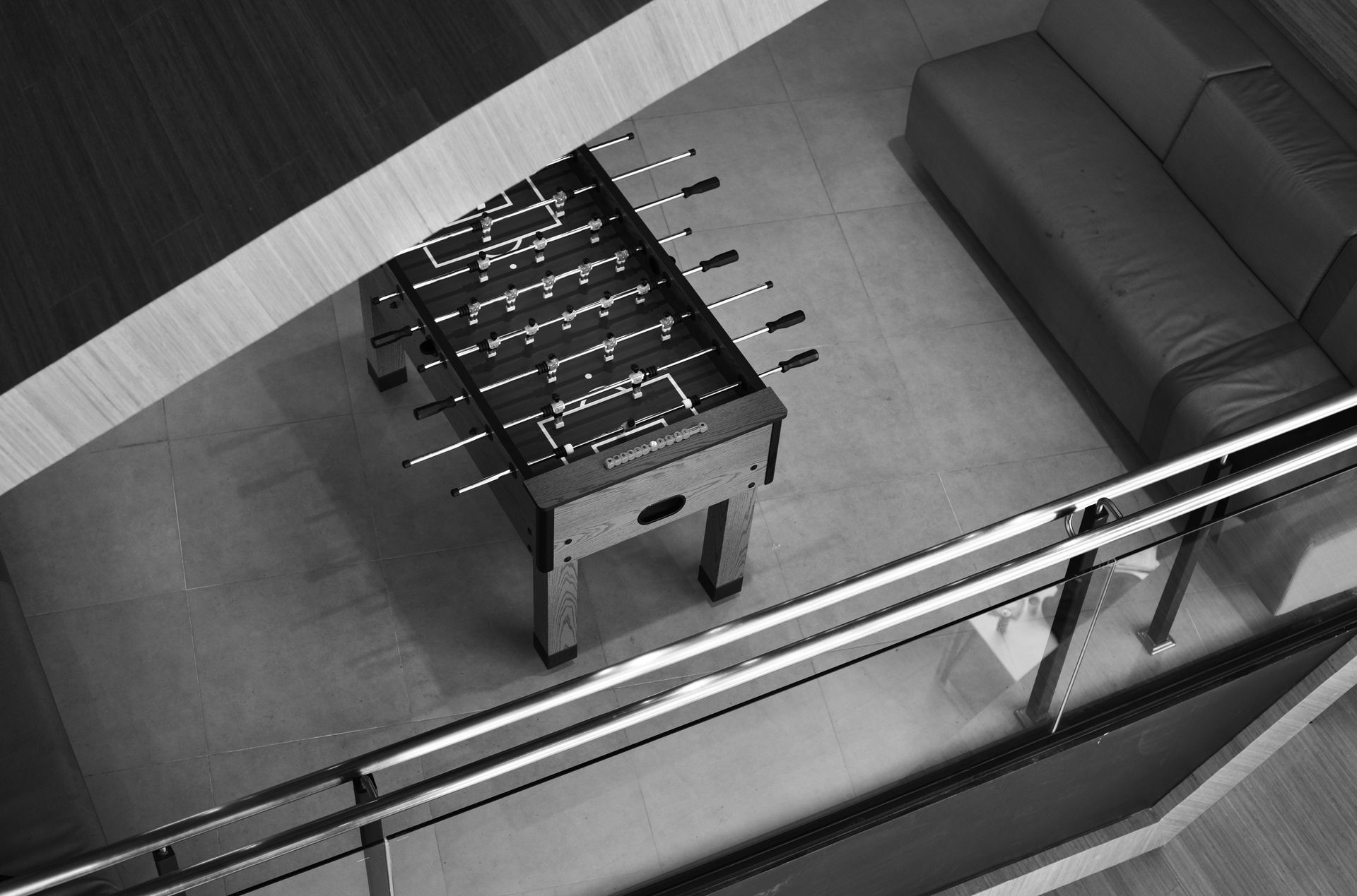 Foosball table in a modern interior setting with a dark couch, and a railing.