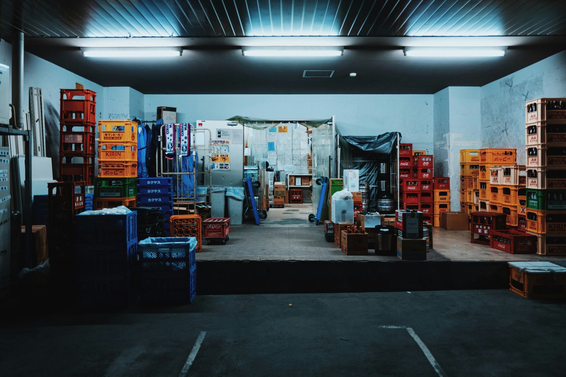 Warehouse interior with stacks of colorful crates, storage area, and fluorescent lights.