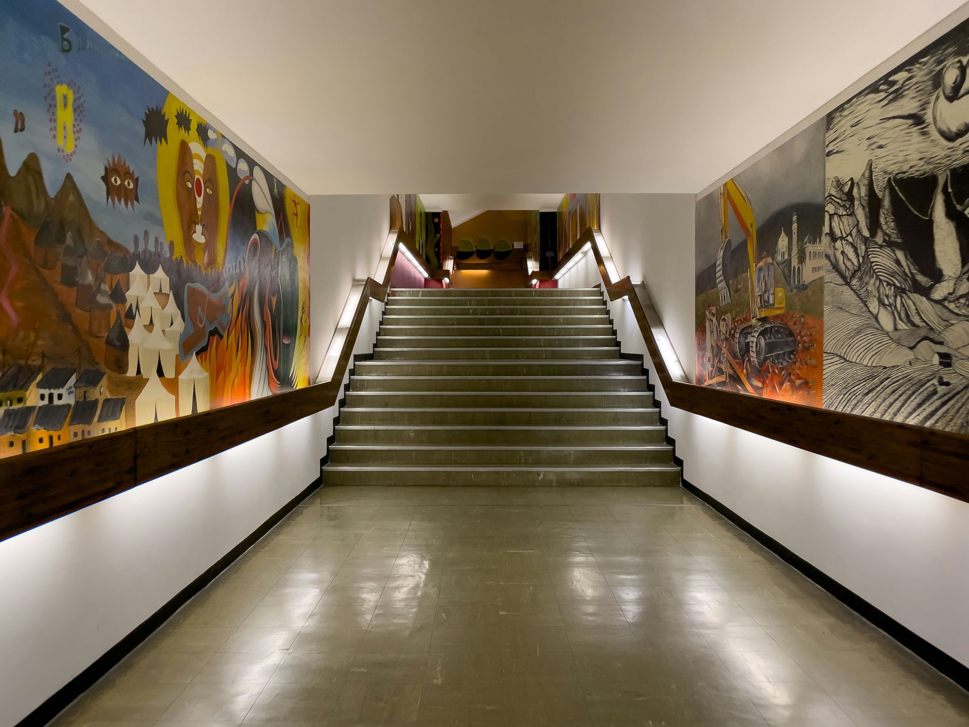 Hallway with a staircase lined by colorful murals and recessed lighting.