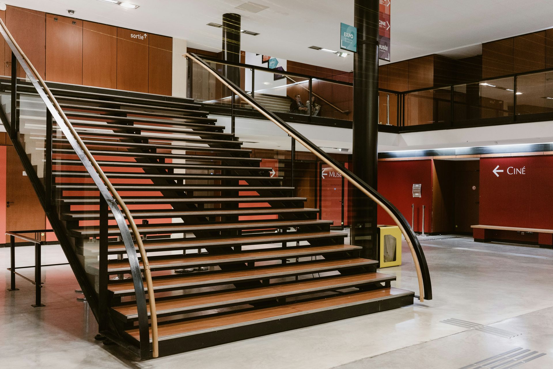Wooden staircase in a building with black railings and brown walls.