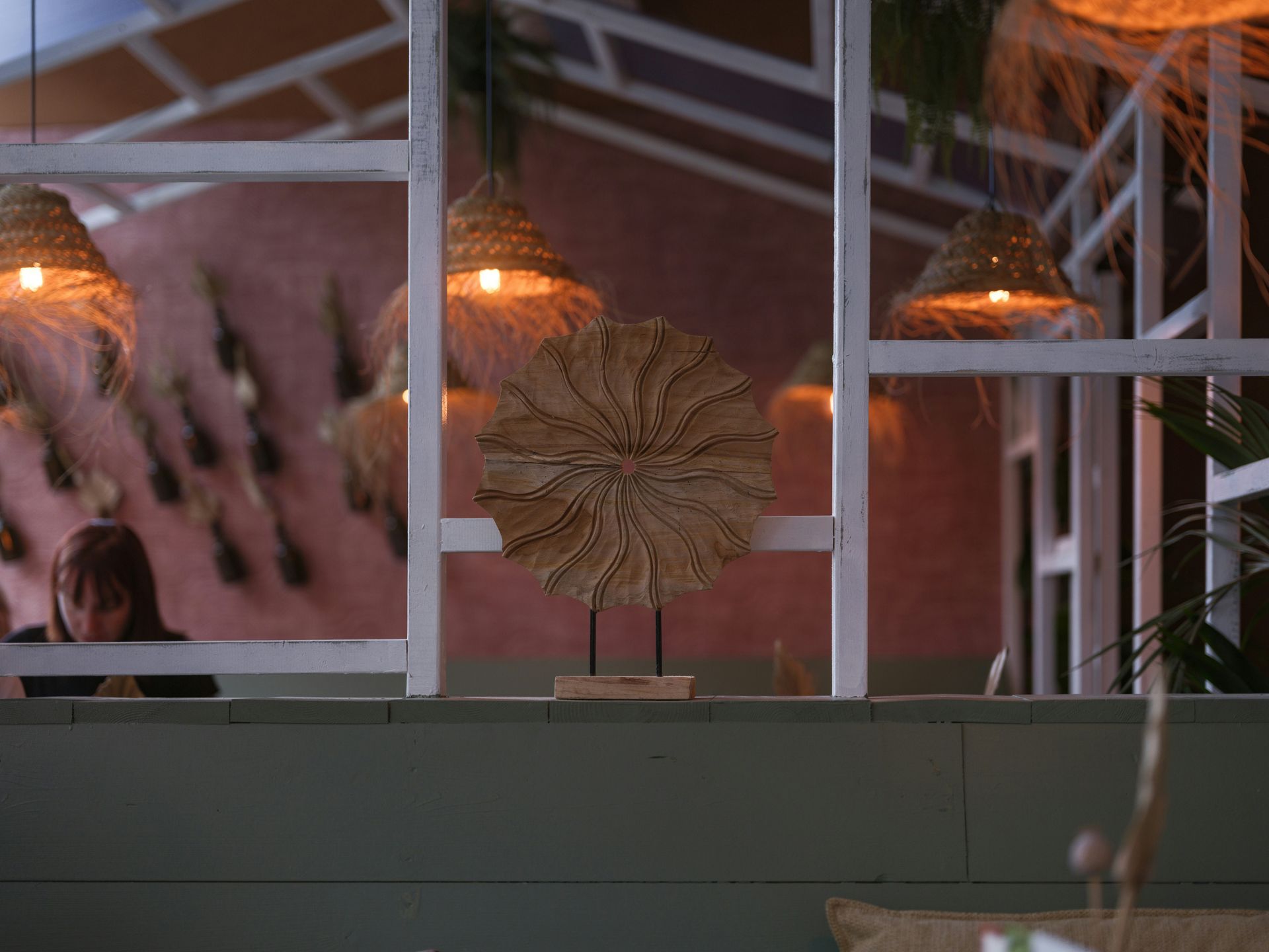 Interior with decorative lighting, a woven fan, and a person working on a laptop.
