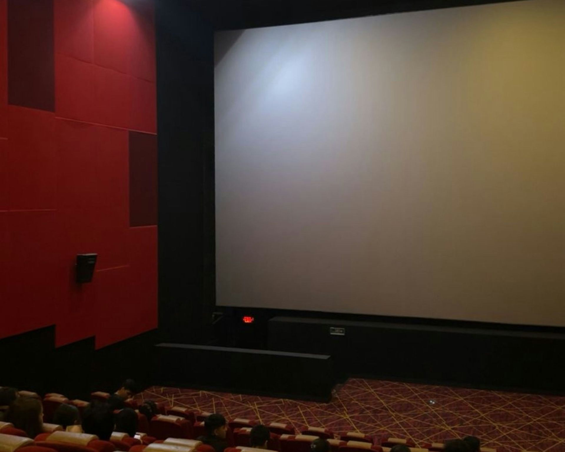 Empty movie theater screen, red wall, and rows of seats.