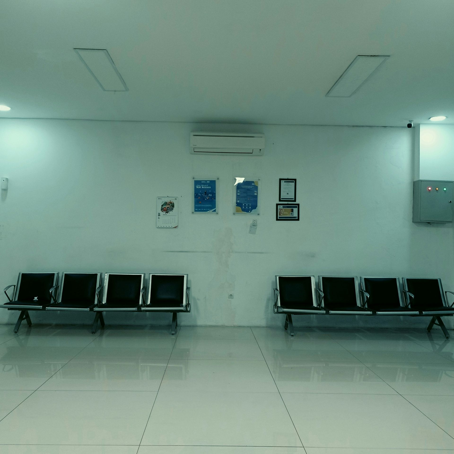 Empty waiting room with black seating, white walls, and bright overhead lights.