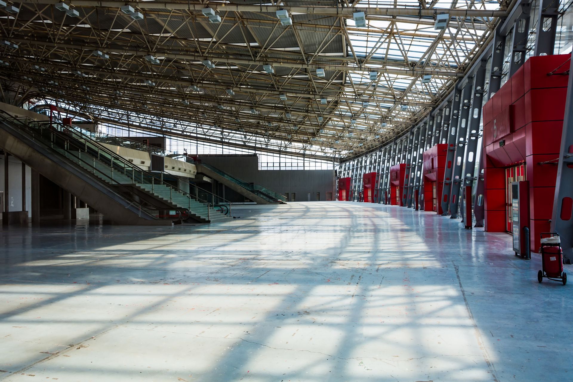 Empty, bright, open-plan exhibition hall with a high ceiling, stairs, and red pillars.