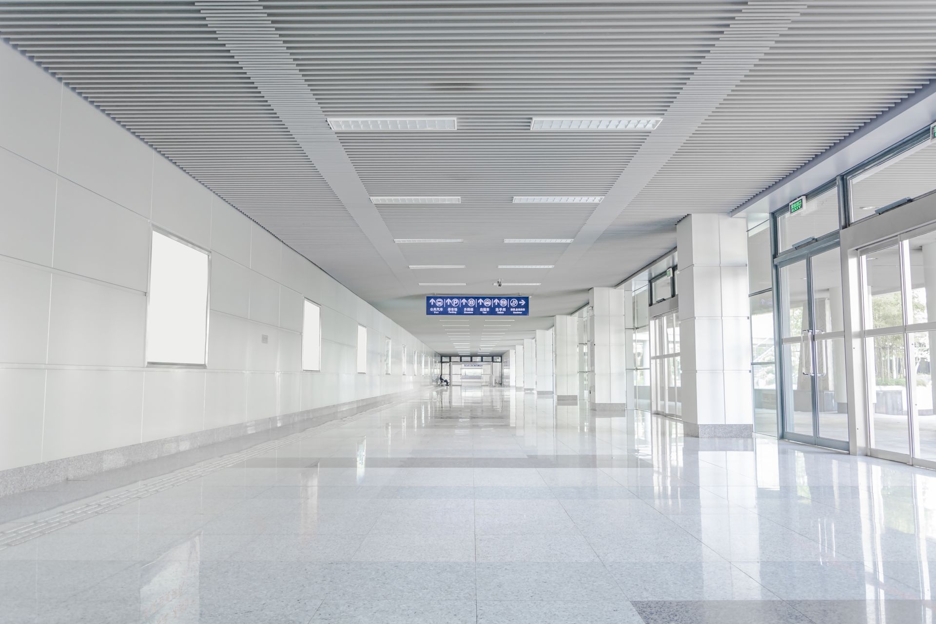 Brightly lit hallway with white walls and glossy floor, leading to glass doors at the end.