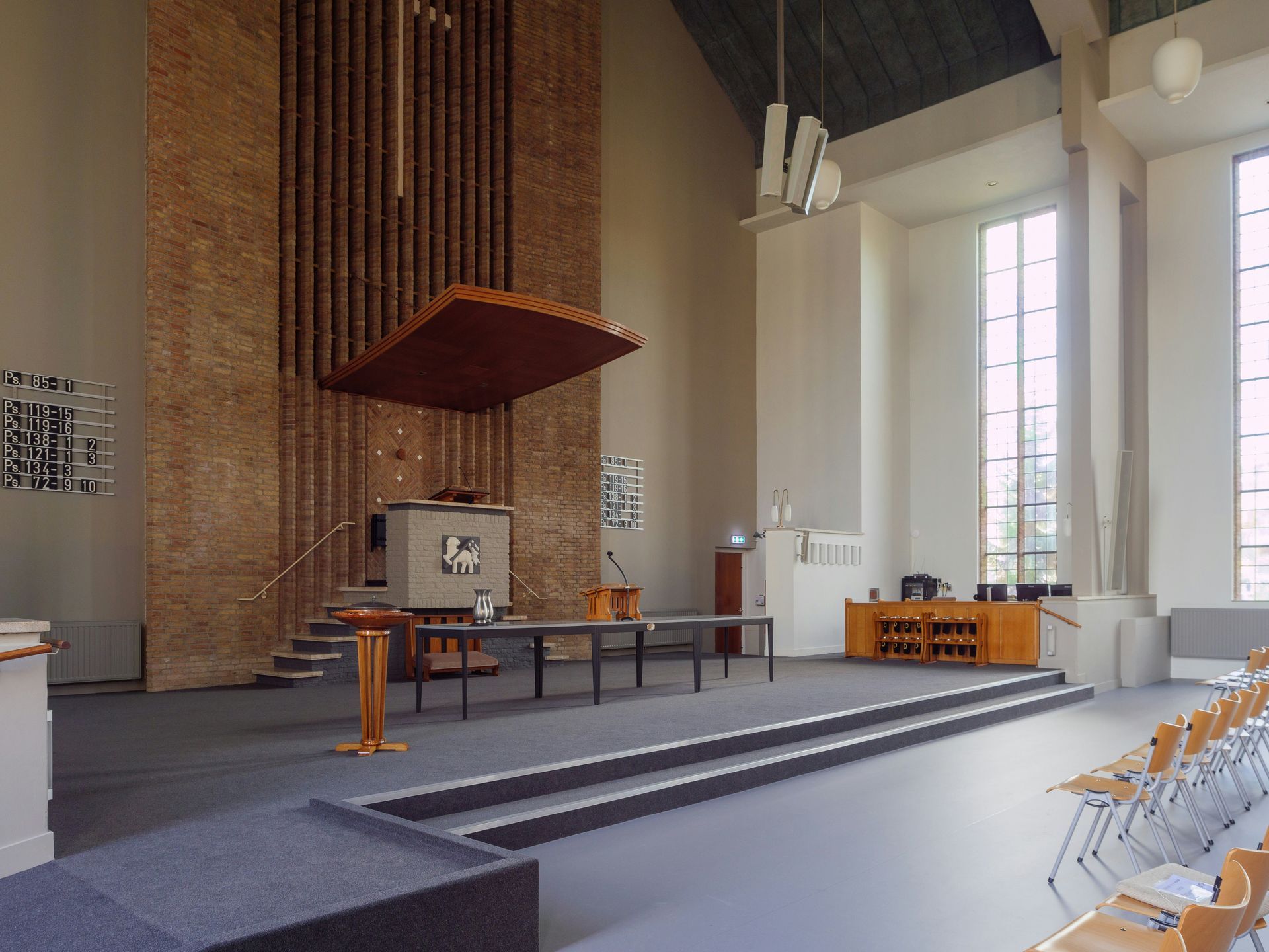 Interior of a church with a brick wall backdrop, altar, and rows of chairs.