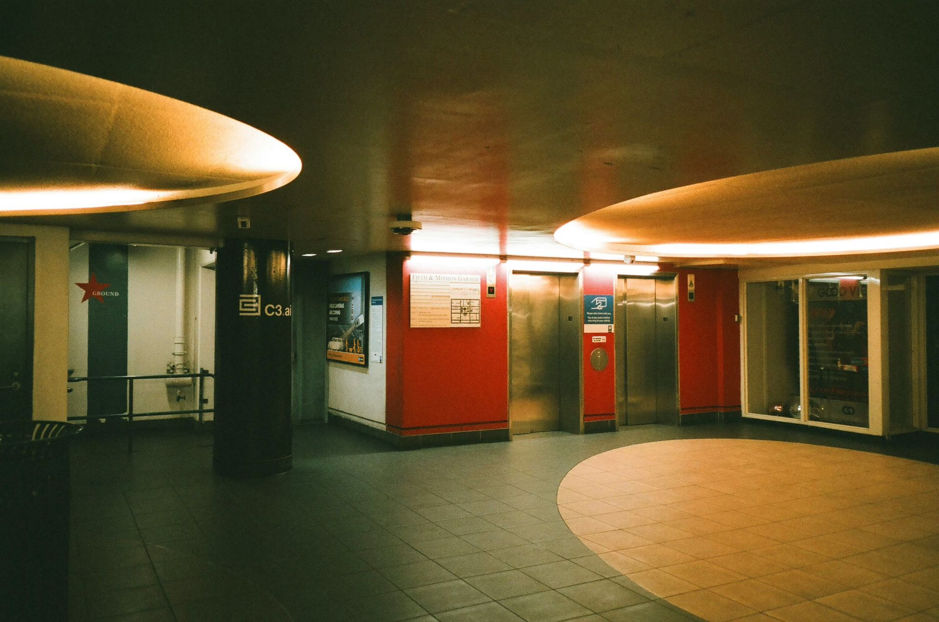 Interior view of a modern building lobby with red walls, elevators, and curved ceiling lights.