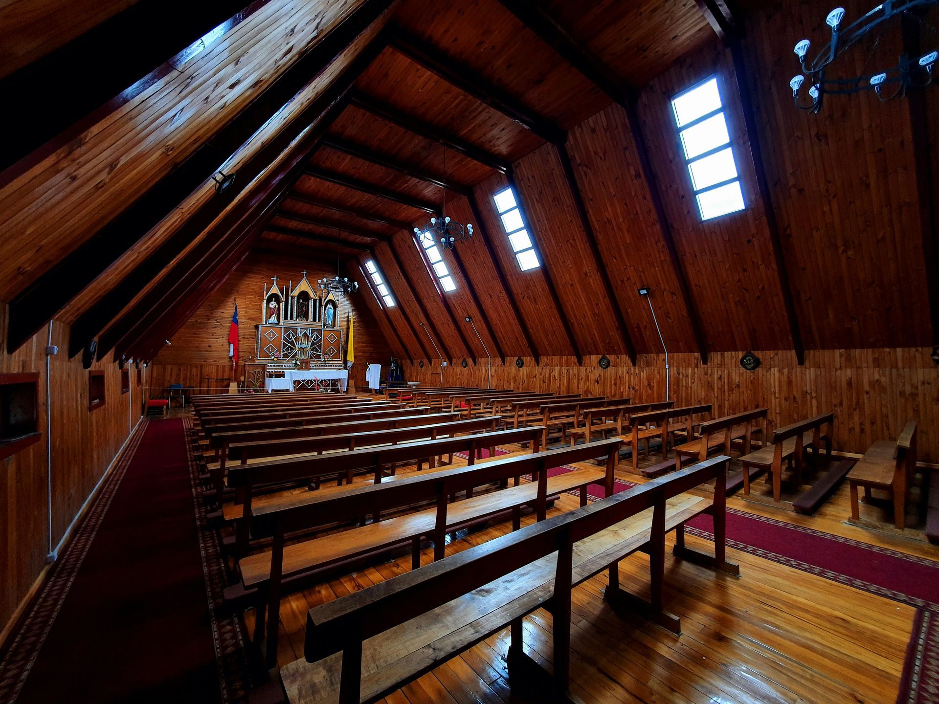 Interior of wooden church with rows of benches leading to an altar. Sunlight streams through high windows.