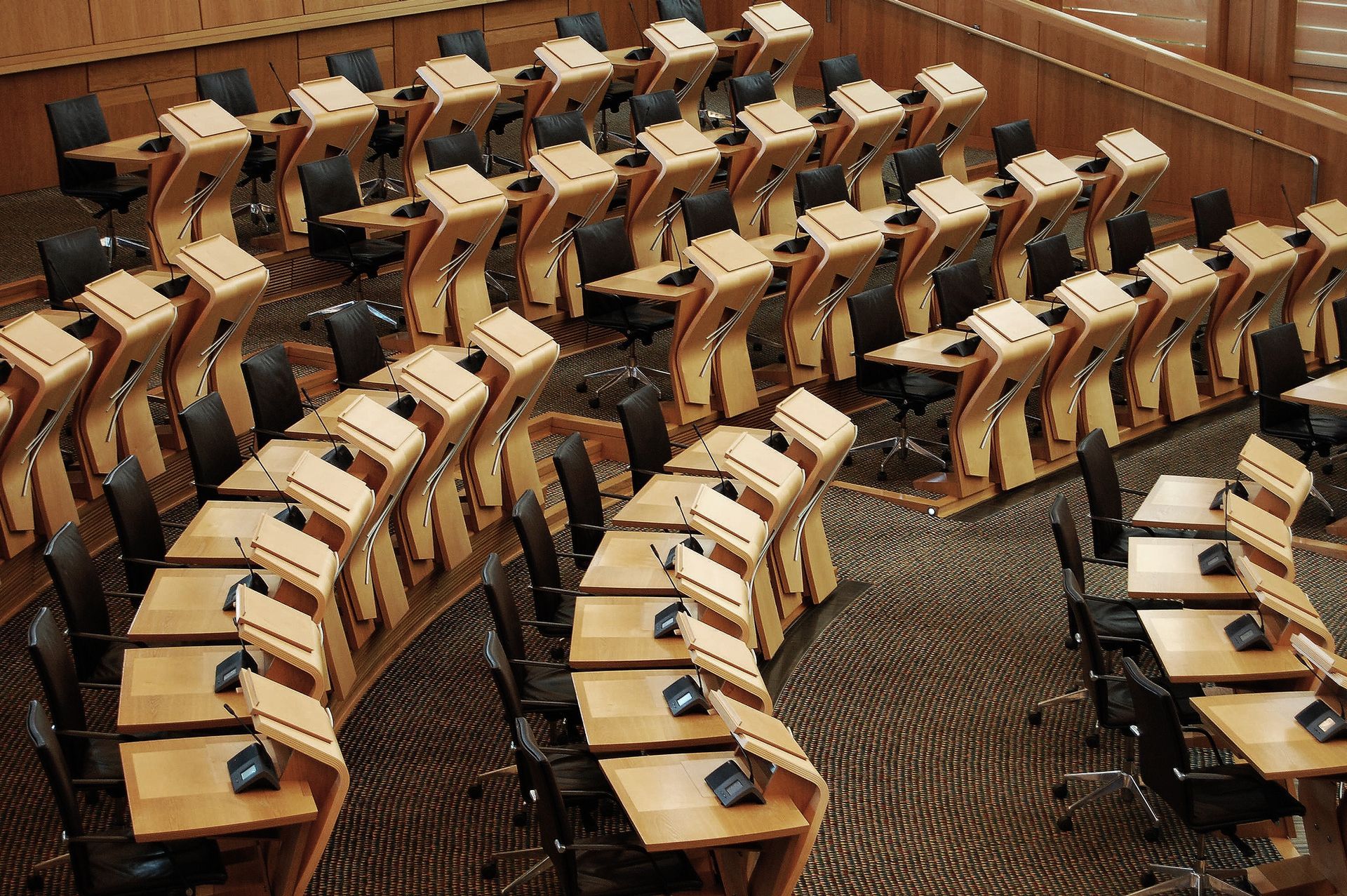 Rows of curved wooden desks and chairs in a large empty auditorium.