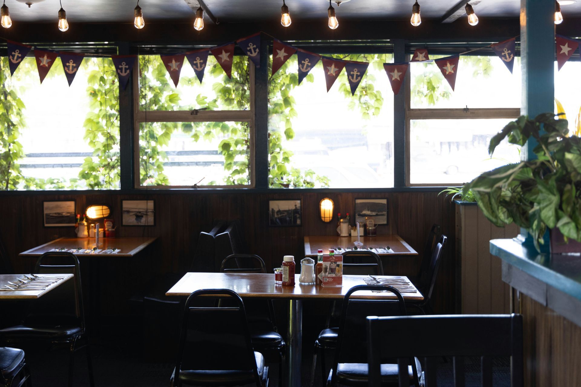 Interior of a restaurant with tables, chairs, and large windows with nautical flags.