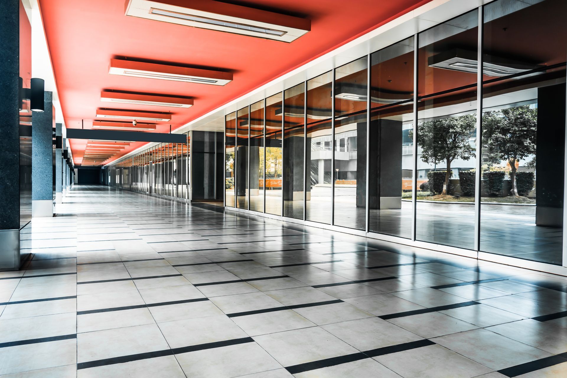 Hallway with large windows reflecting outdoor trees; red ceiling, patterned floor.